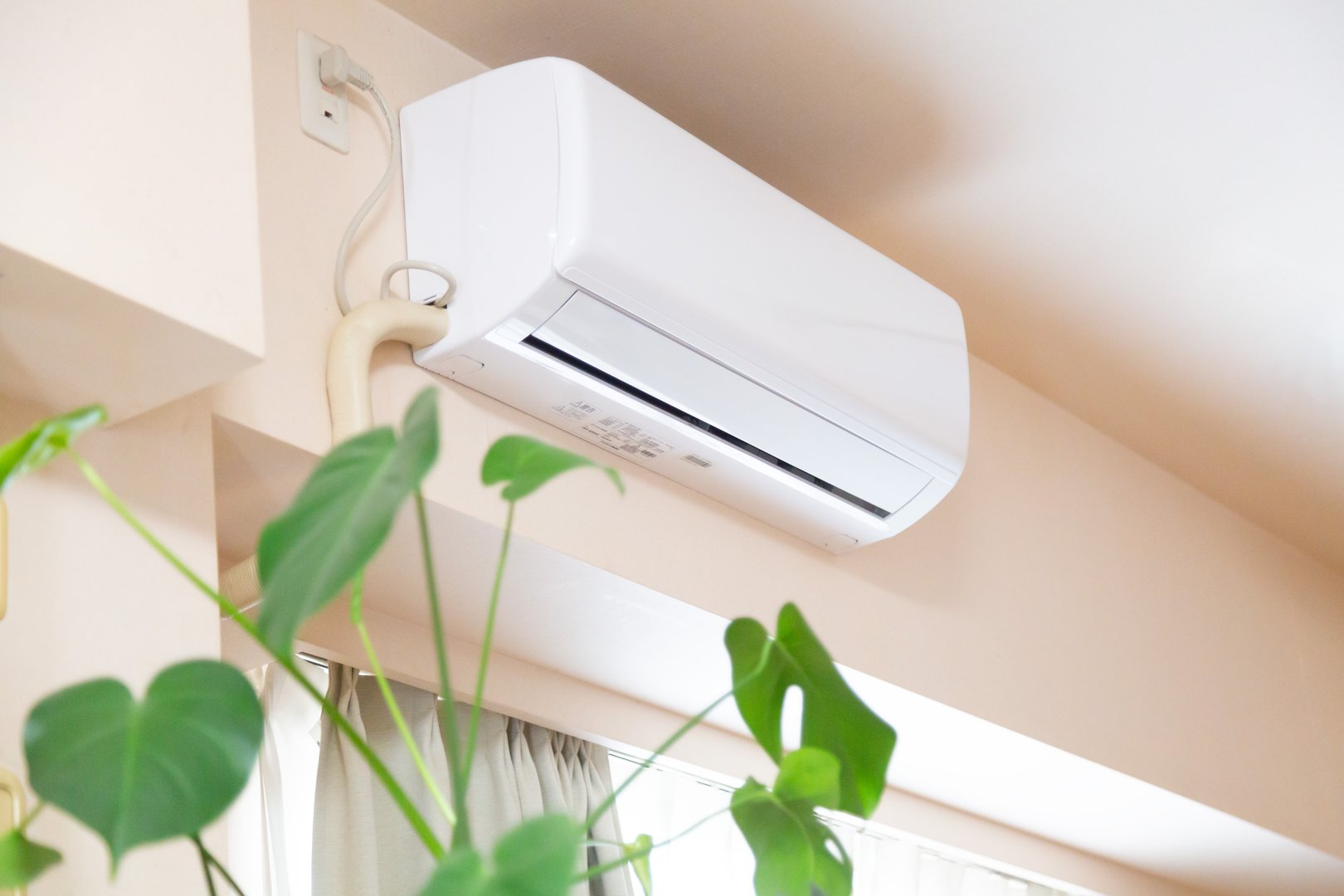 Home appliance air conditioner and green plant leaves at home. Use of air conditioner has been encouraged by the government and medical doctors to cool the room temperature down in order to avoid heat stroke risk due to the effect of global warming and climate change.
