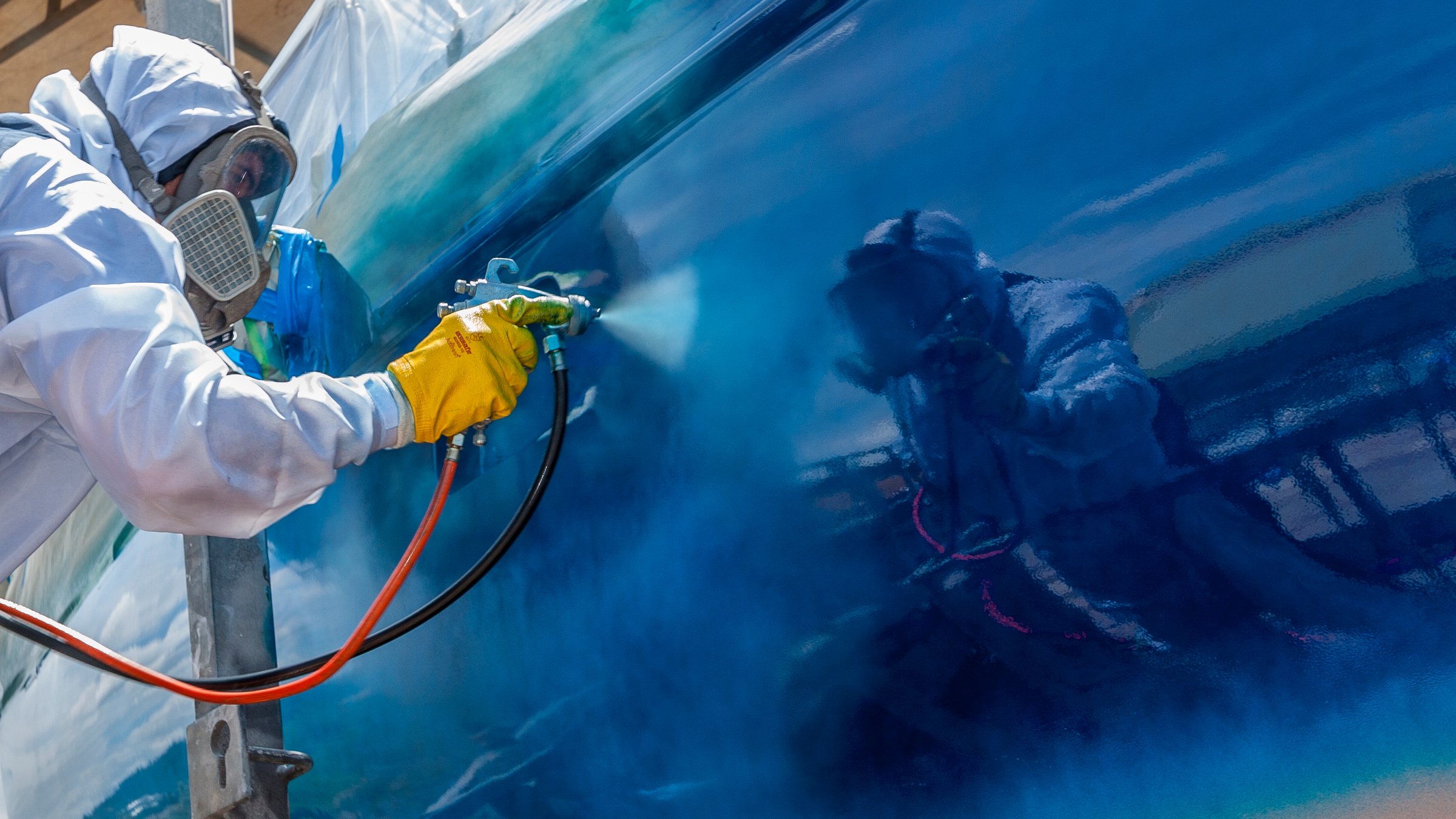 Spray painter with full body protection and mask painting the hull of sailboat