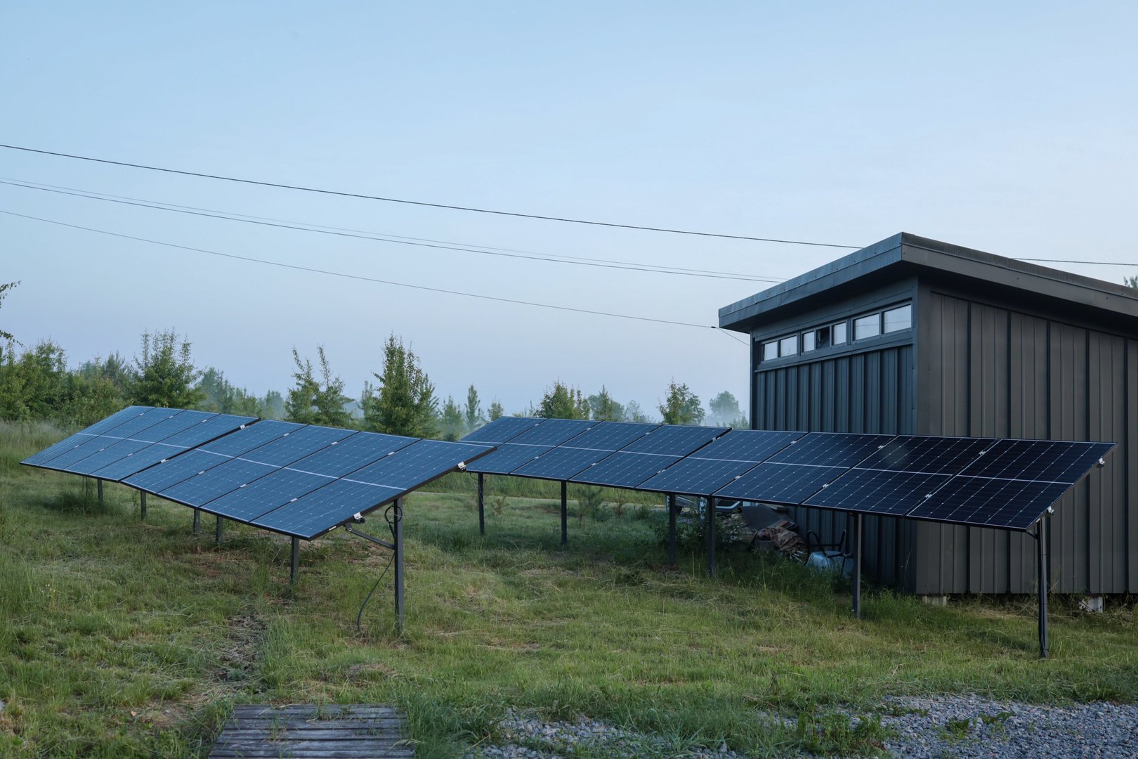 Solar panel installations beside a modern utility building in a green field, generating renewable energy on a sunny day.