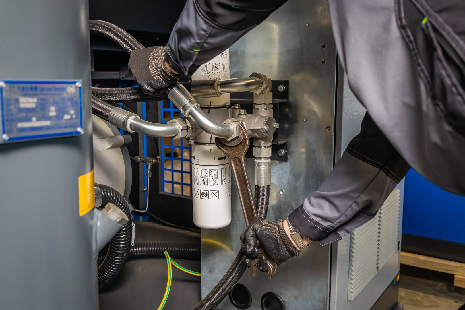 Close up of a technician tightening a pipe fitting on an industrial air compressor during maintenance