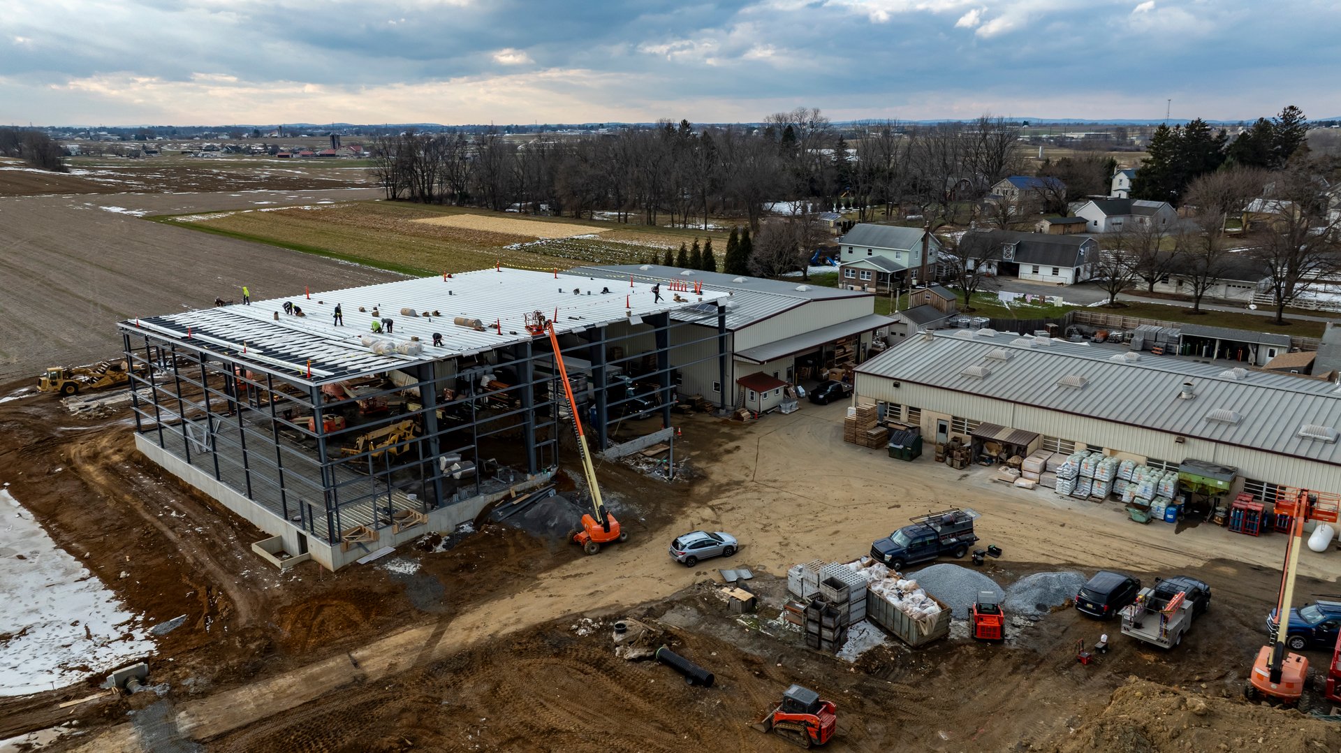 Workers are actively constructing a large facility in a rural setting. Heavy machinery is in use, showcasing the development of the building and surrounding area.