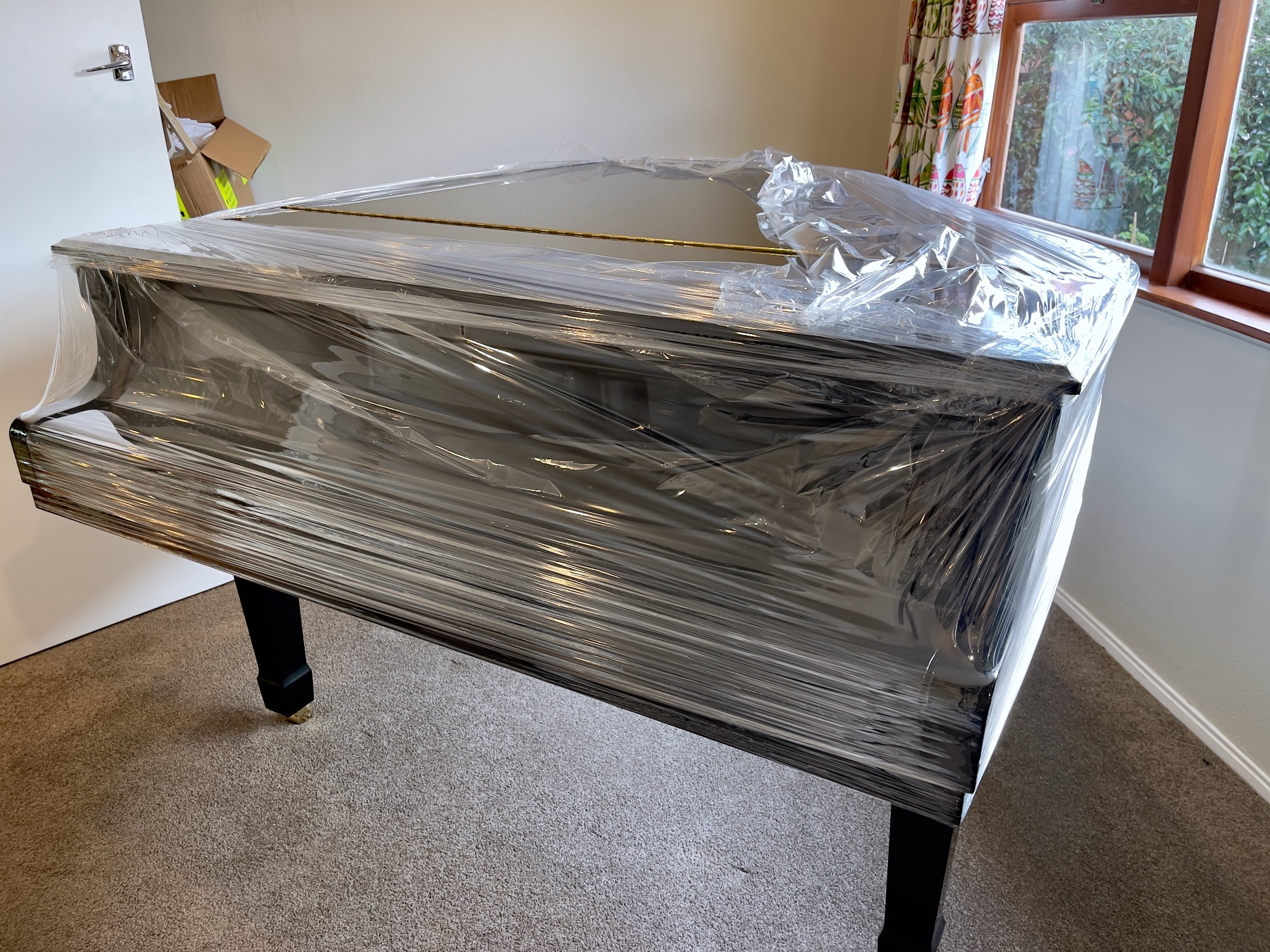 Large ebony piano wrapped in cling film to protect against scratches while being transported