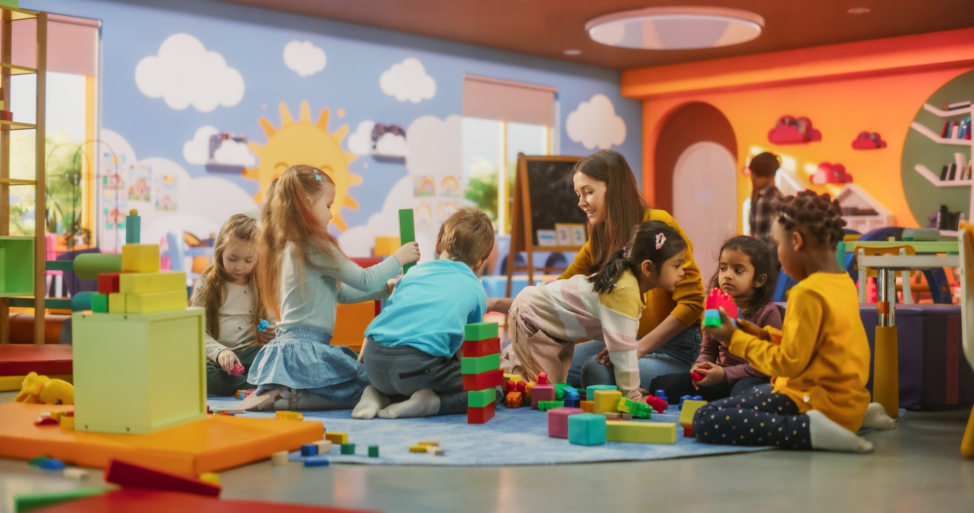 Cheerful Diverse Kids Playing with Colorful Building Block Toys in Kindergarten. Group of Multiethnic Boys and Girls Playing Together with a Female Teacher in a Modern Daycare Center