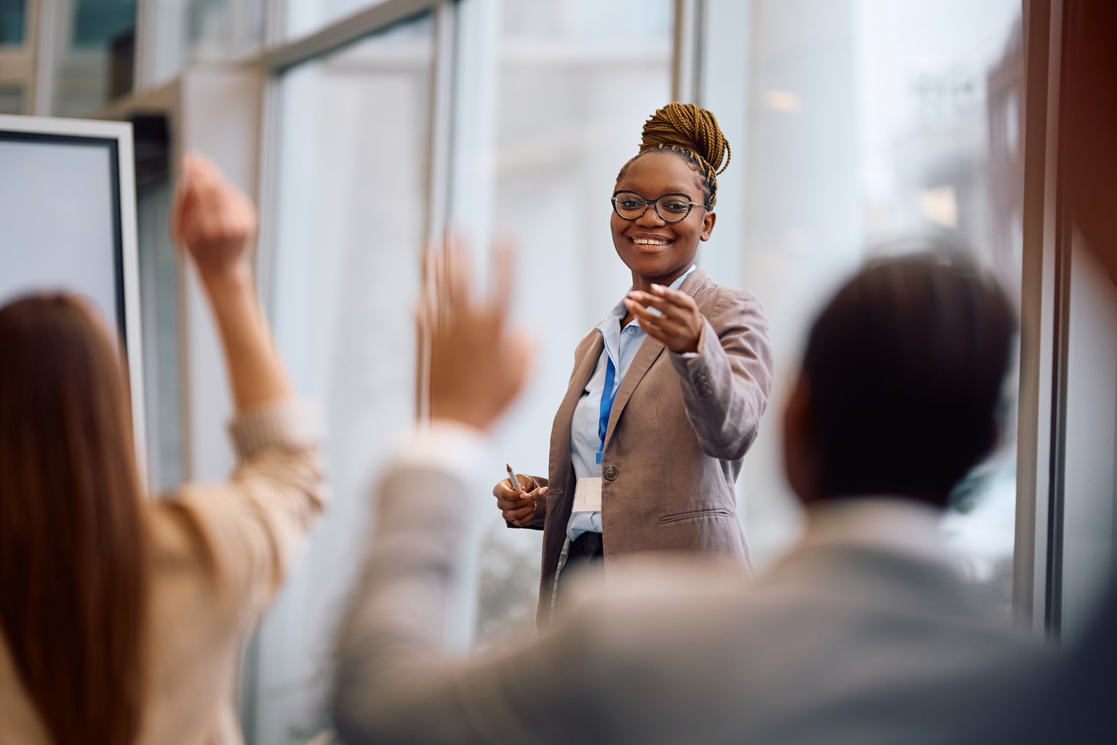 Happy African American businesswoman aiming at one of colleagues who wants to ask a question during a conference in board room.