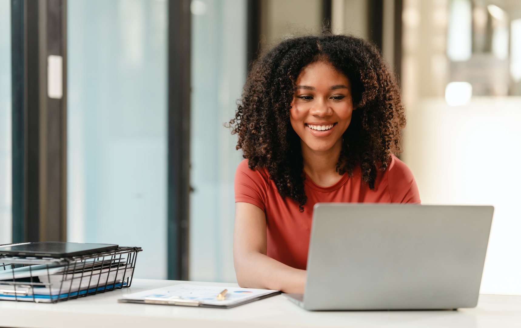 Portrait of joyful African American woman people with an afro hairstyle, working on a laptop at a desk with documents.