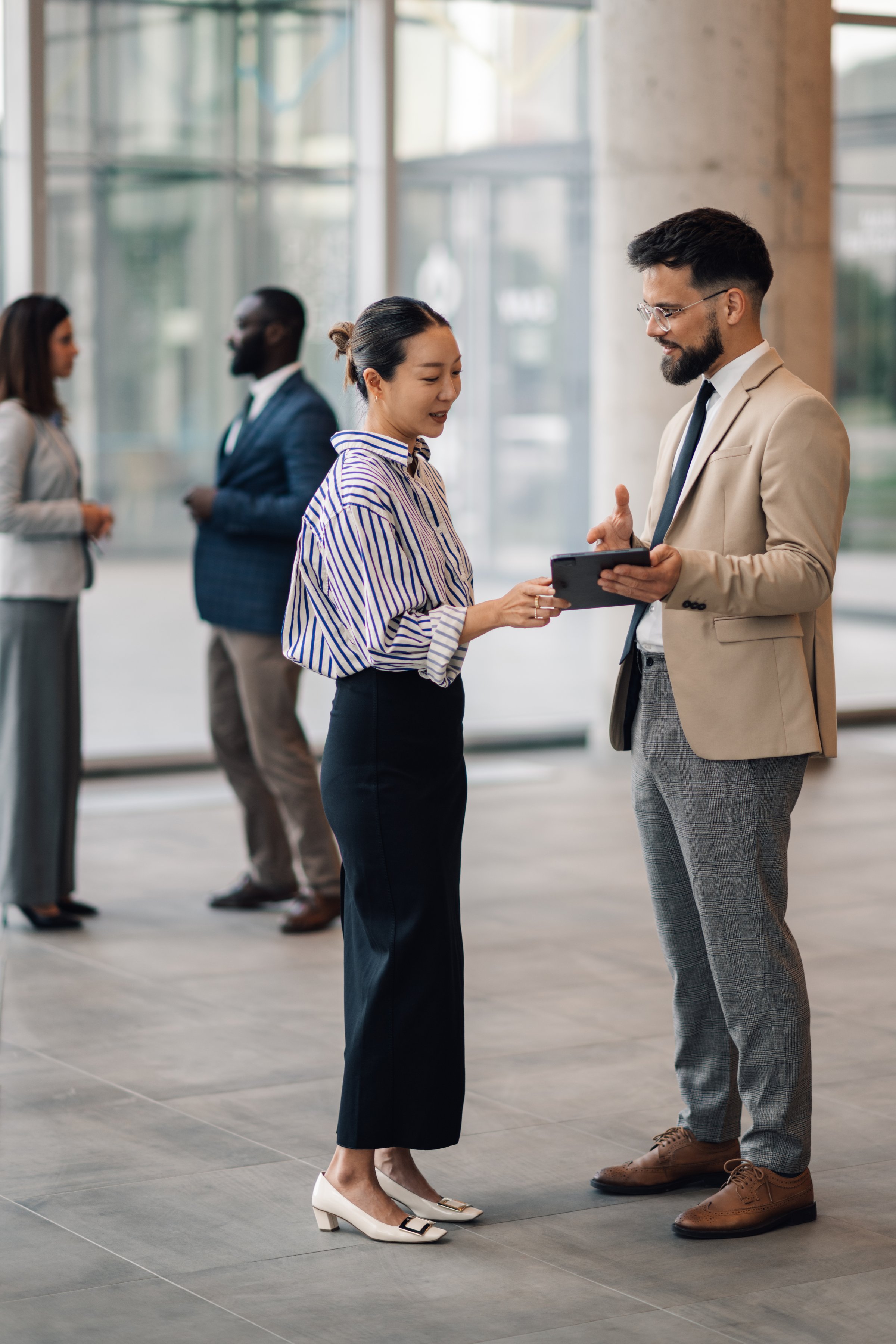 Business colleagues engaging in discussion while using a digital tablet in a modern office lobby, fostering teamwork and collaboration