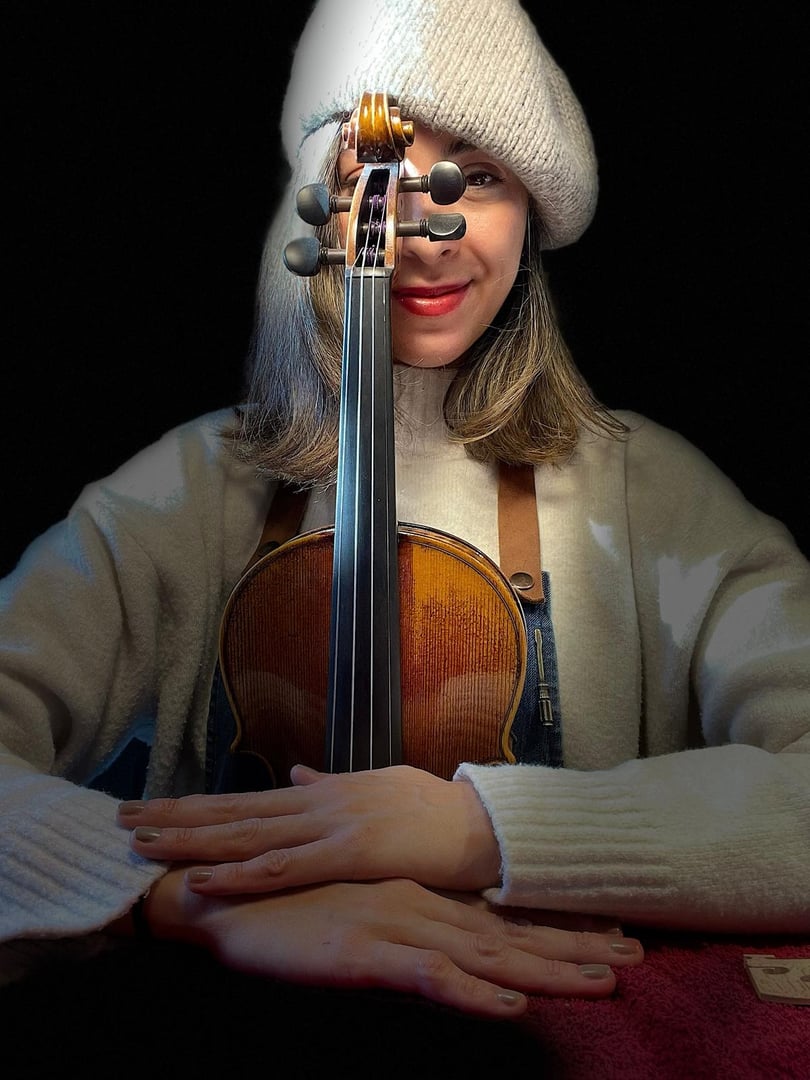 Luthier carefully applying varnish on a violin with brush and finger, showcasing the delicate process of antiquing and restoring stringed instruments in a traditional workshop environment