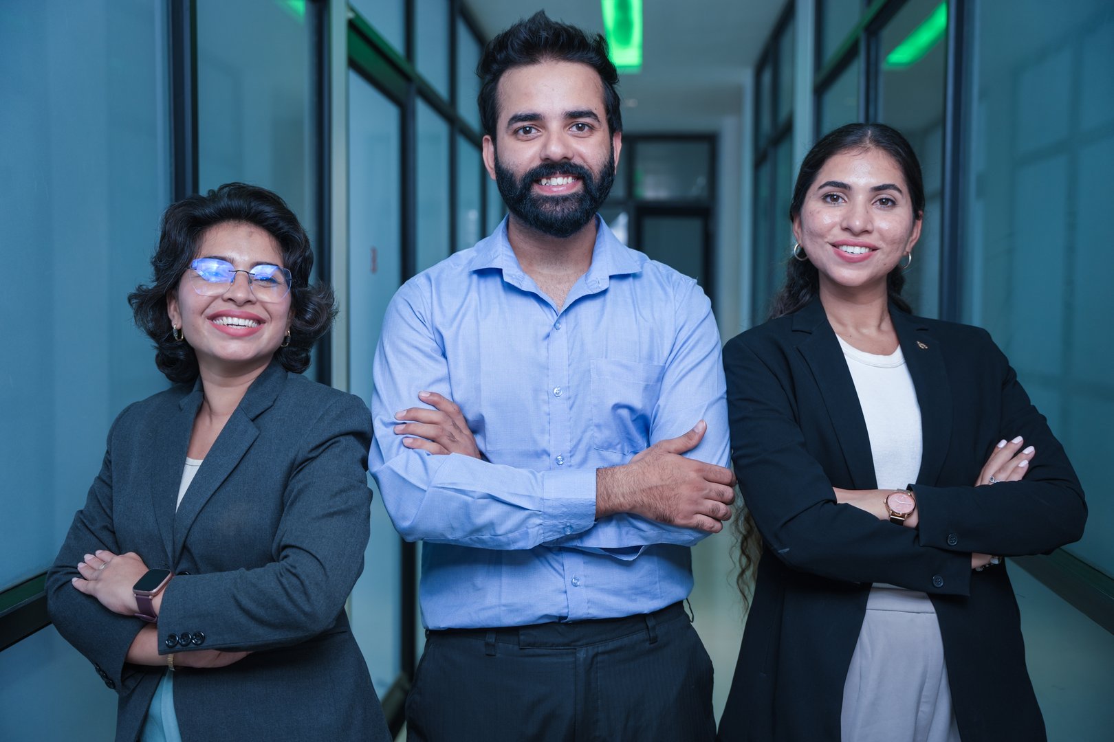 Confident group of three young indian corporate business people in formal wear standing cross arm in office hallway looking at camera. Teamwork, unity, and workplace concept.