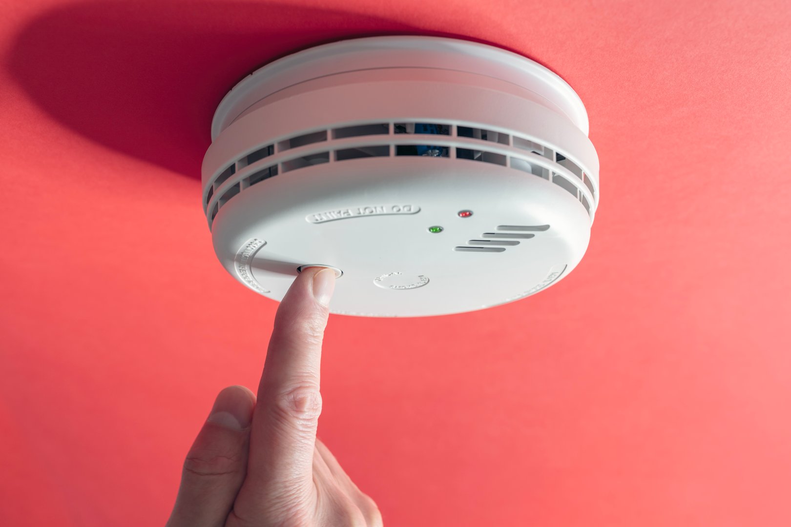 Home smoke and fire alarm detector maintenance man pushing button checking, testing or replacing battery