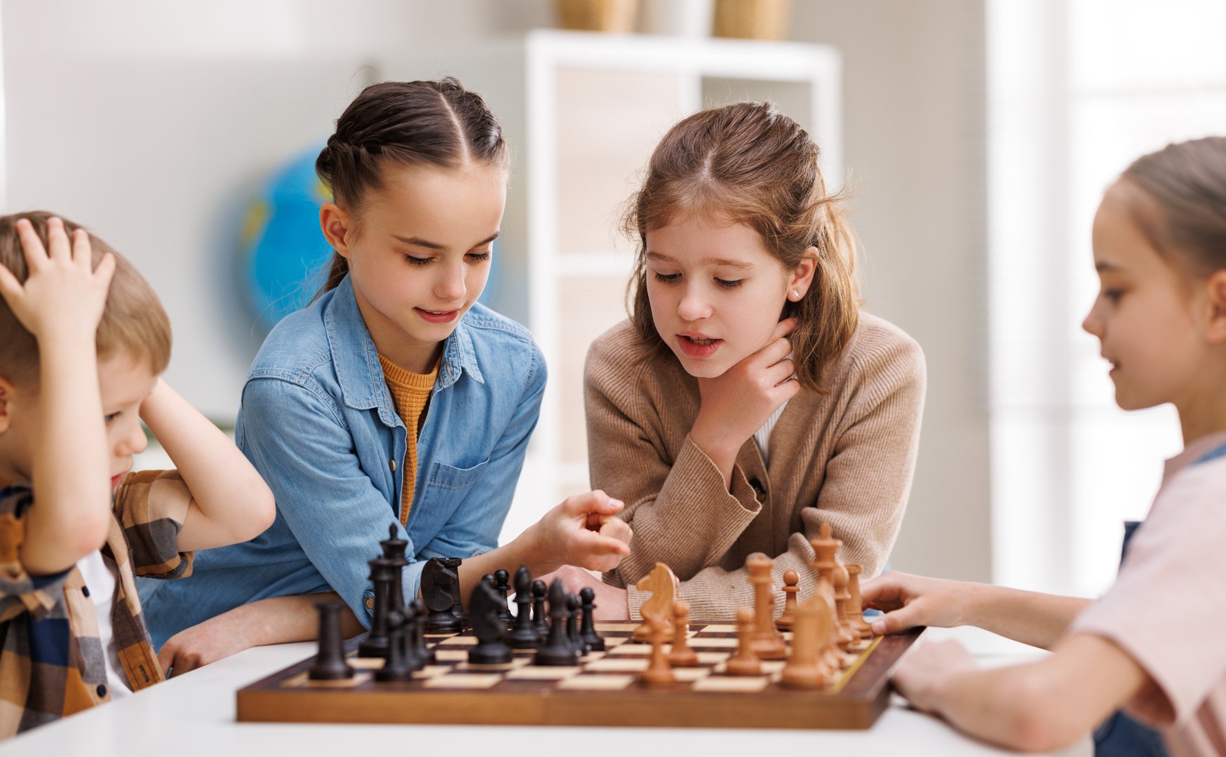 Little classmates gathering around table and pondering over move while learning to play chess during lesson at school