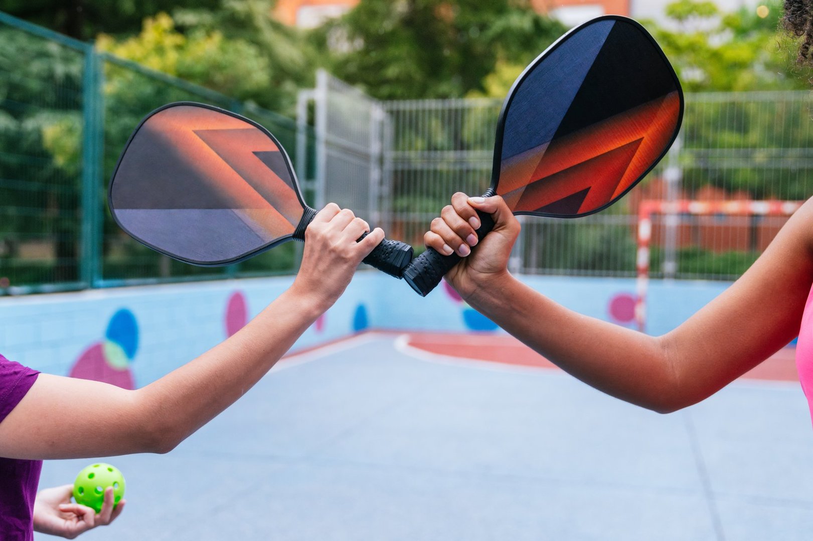 Two multiethnic female athletes prepare to play pickleball, holding their rackets together on the court