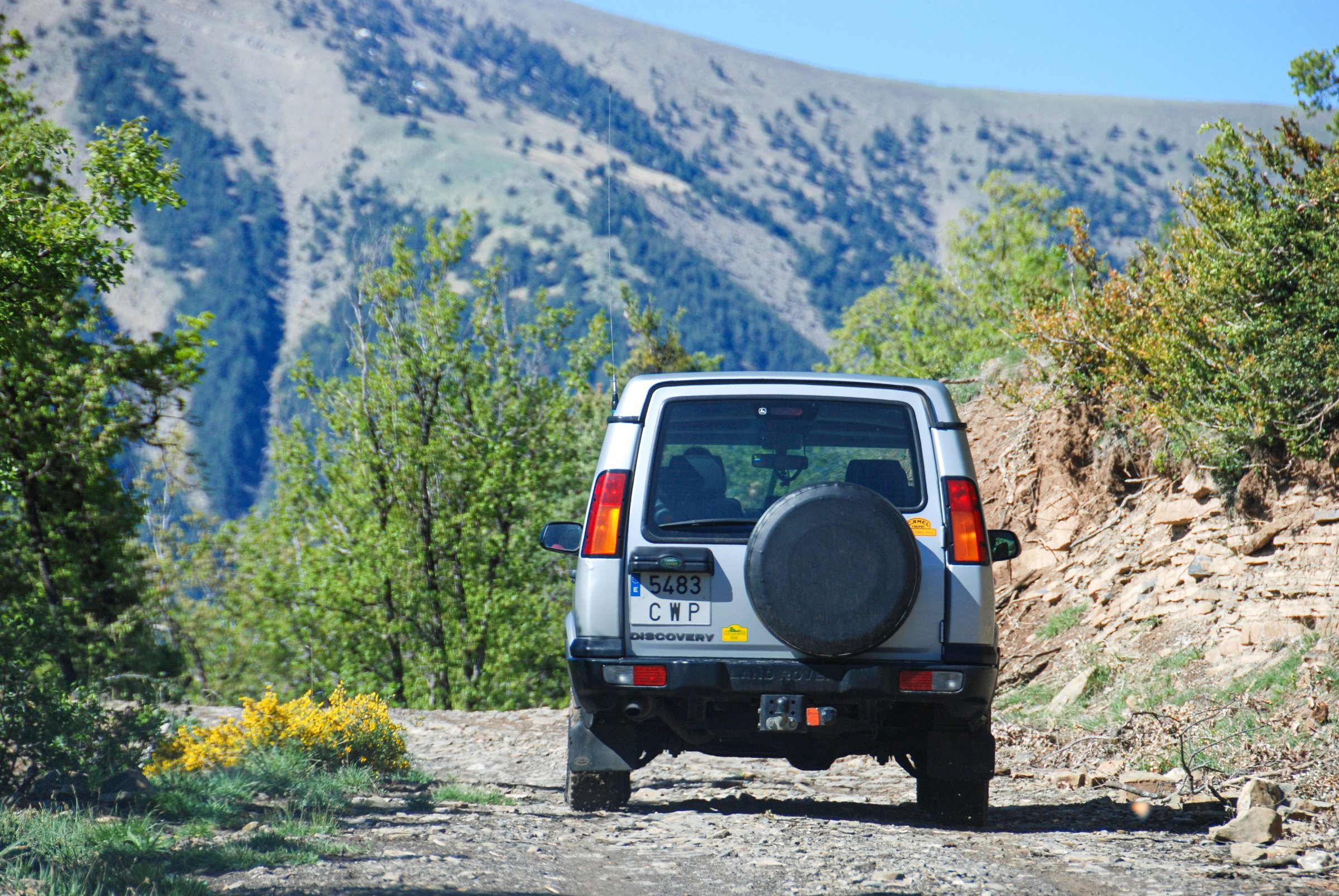 Huesca, Spain, Pyrenees, 05/06/2017 Discovery two, land rover, seen from the rear, is heading towards the mountains, towards the Pyrenees, along a dirt road that climbs through the woods. In the background the blue sky on a spring day