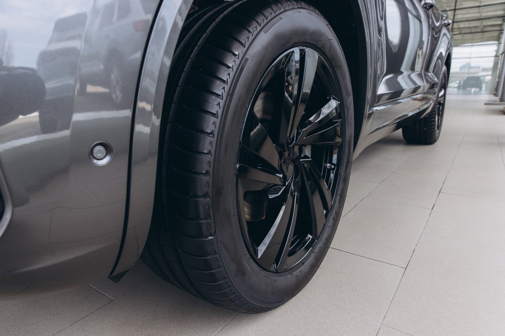 Close up showcasing a black alloy wheel and tire of a gray modern car, emphasizing the vehicle's design and automotive details