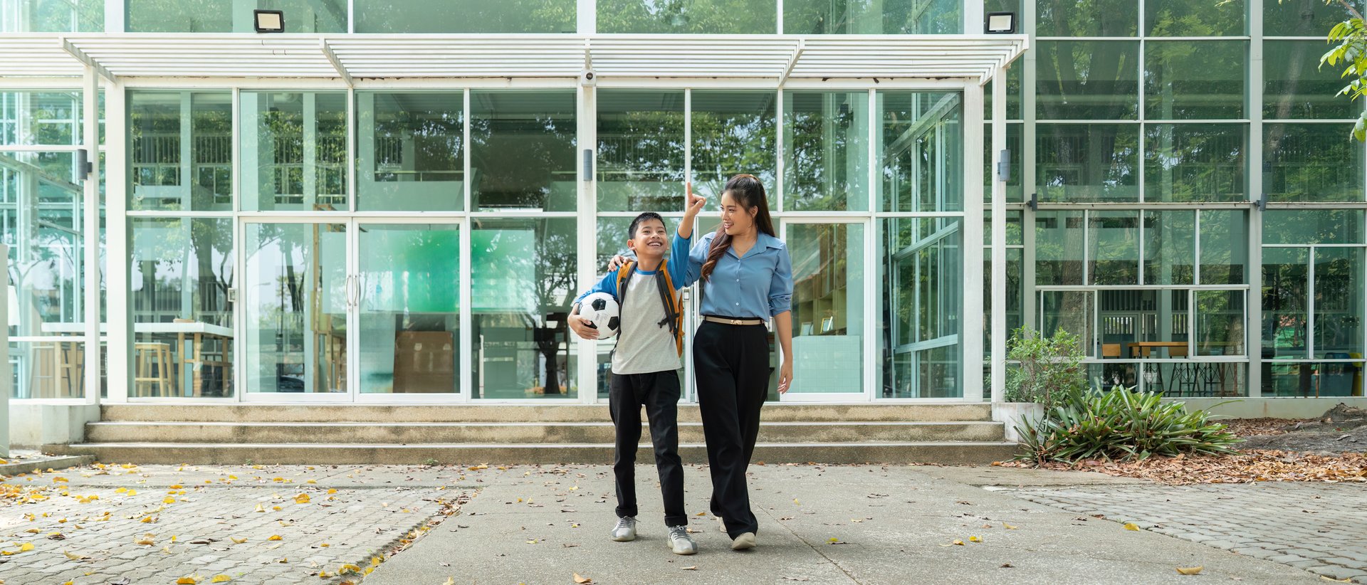 A young boy excitedly walks home with his mentor, holding a soccer ball. Their conversation highlights the joy of returning to school and outdoor activities.