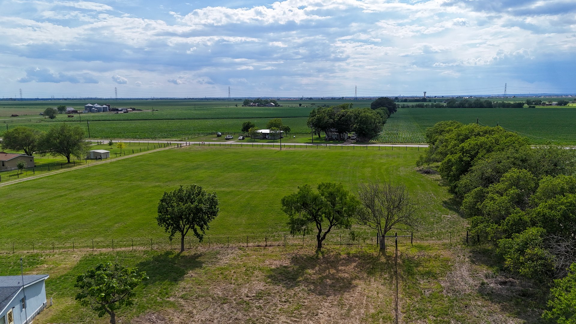 Aerial view of a lush green field surrounded by trees and farmland under a partly cloudy sky.