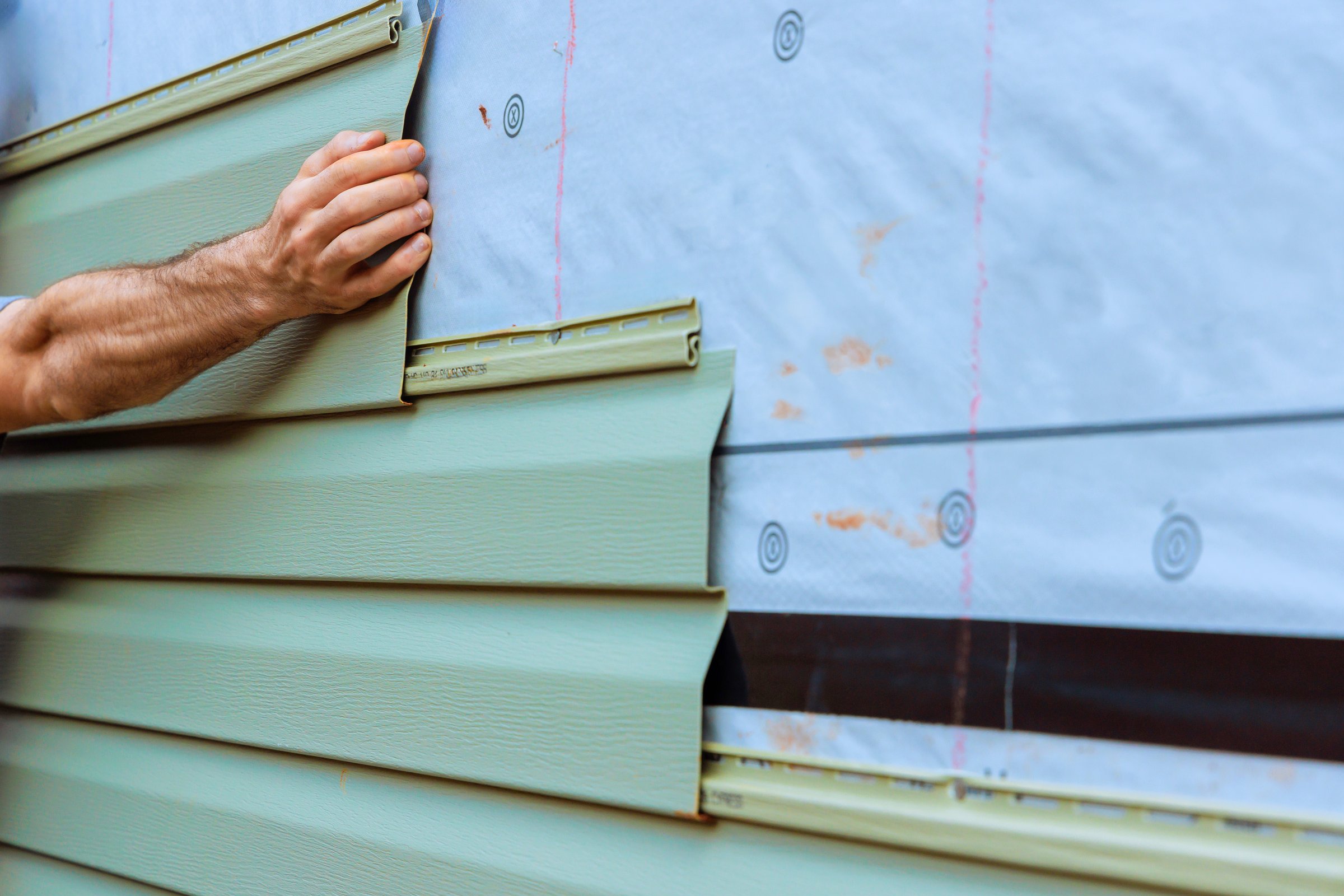 Construction worker carefully fits section of green PVC siding onto wall during home improvement task.