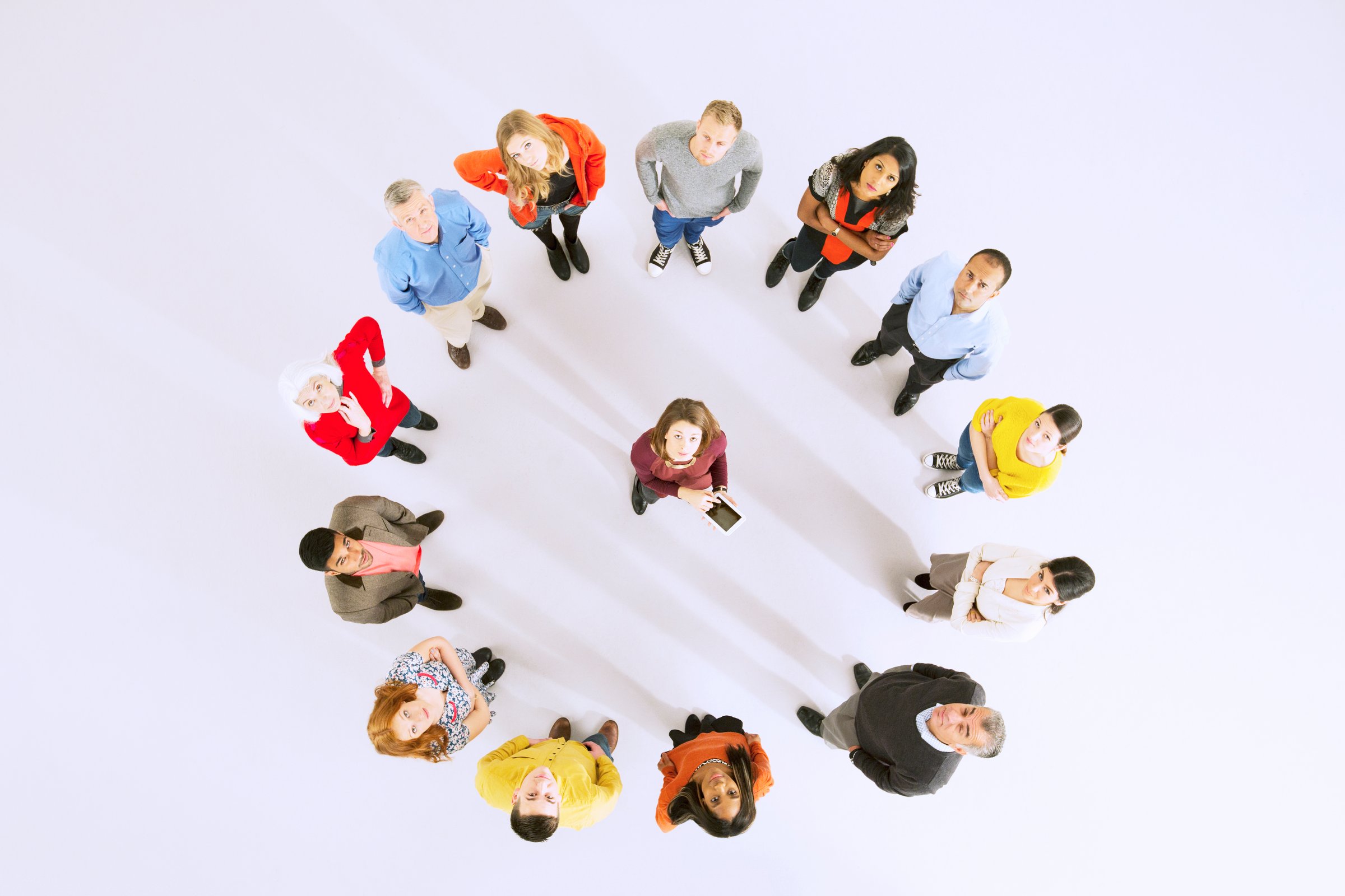 A diverse group of people standing in a circle on a white background, viewed from above. They look towards the center.