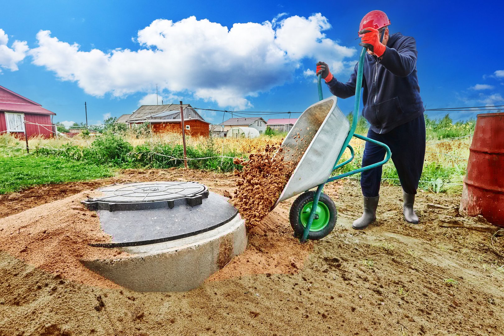 Worker pours sand from wheelbarrow onto concrete ring of septic tank.