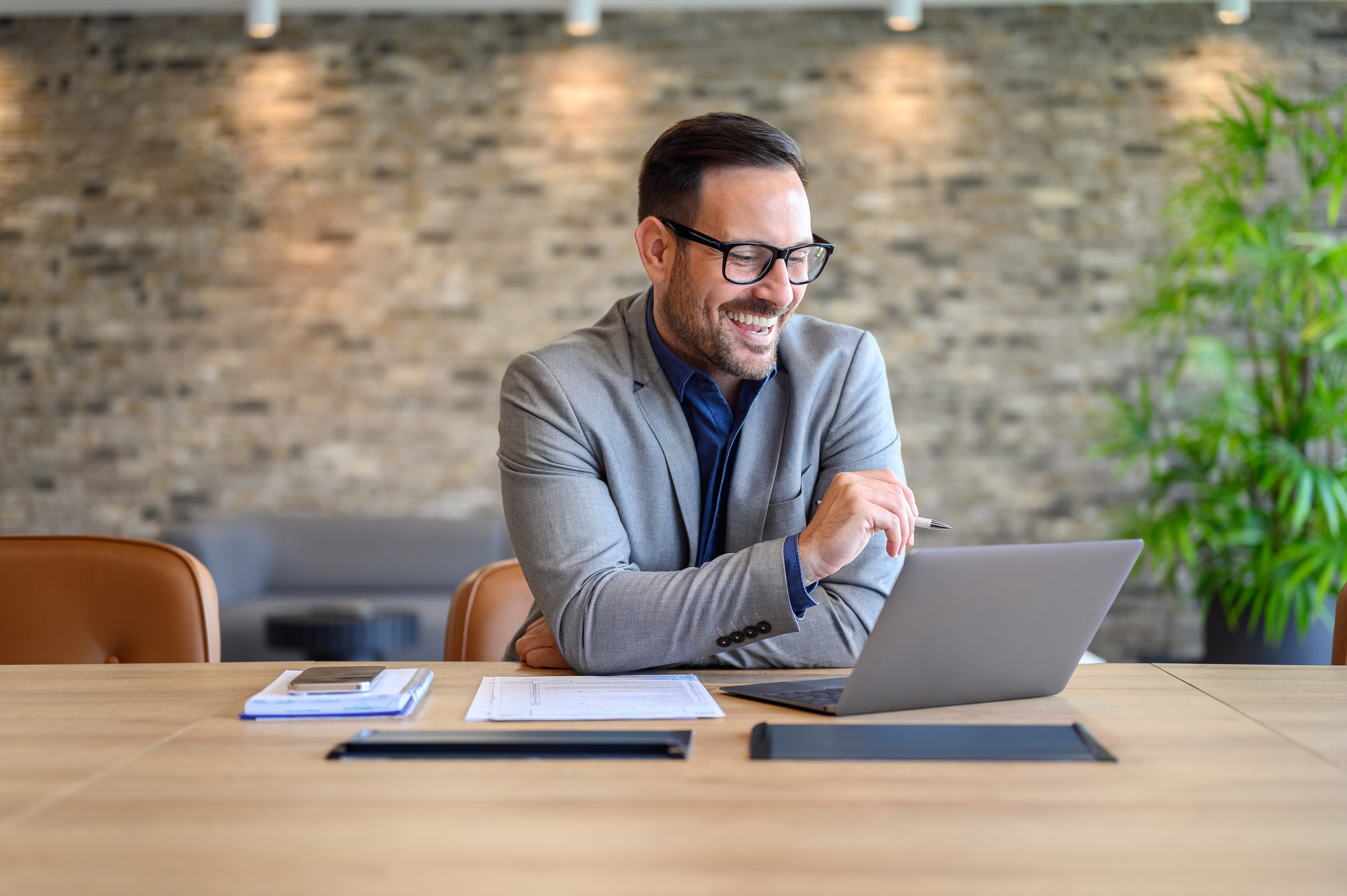 Portrait of cheerful male project manager planning over laptop during online meeting at desk in office
