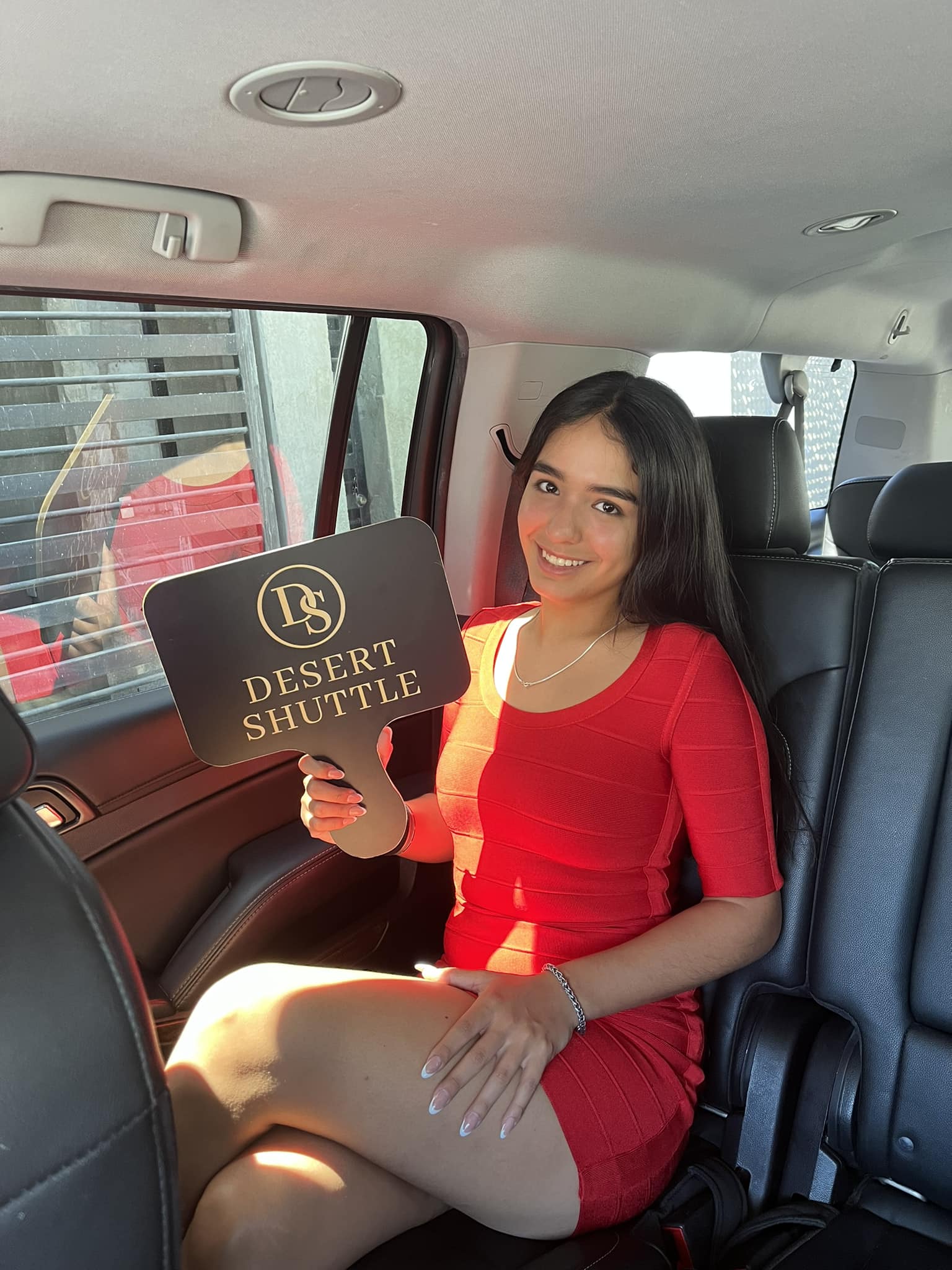 Woman in a red dress sitting in a car holding a Desert Shuttle sign.