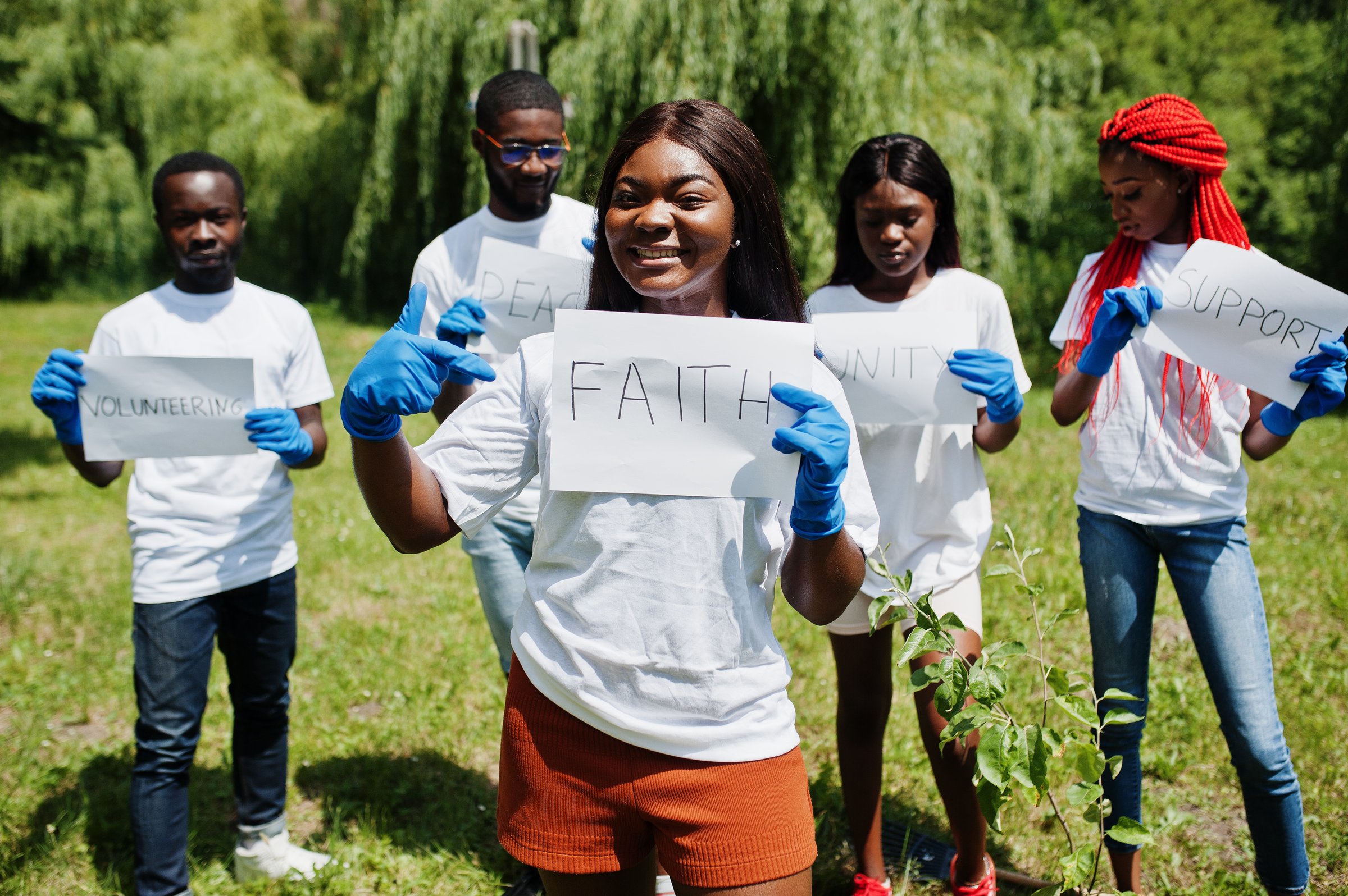 Group of happy african volunteers hold blank board with faith sign in park. Africa volunteering, charity, people and ecology concept.