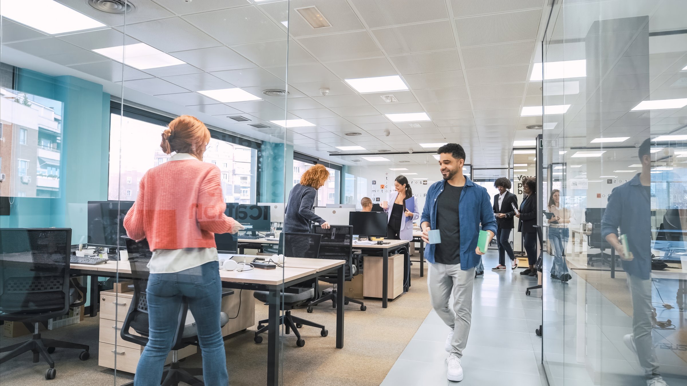 Multiethnic business colleagues walking into creative workspace with computer desks in bright office