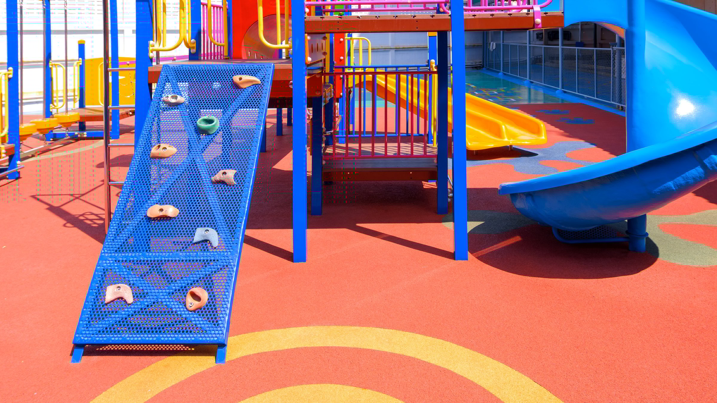 Slide and jungle gym playground equipment on colorful rubber floor in outdoors playground area of kindergarten school