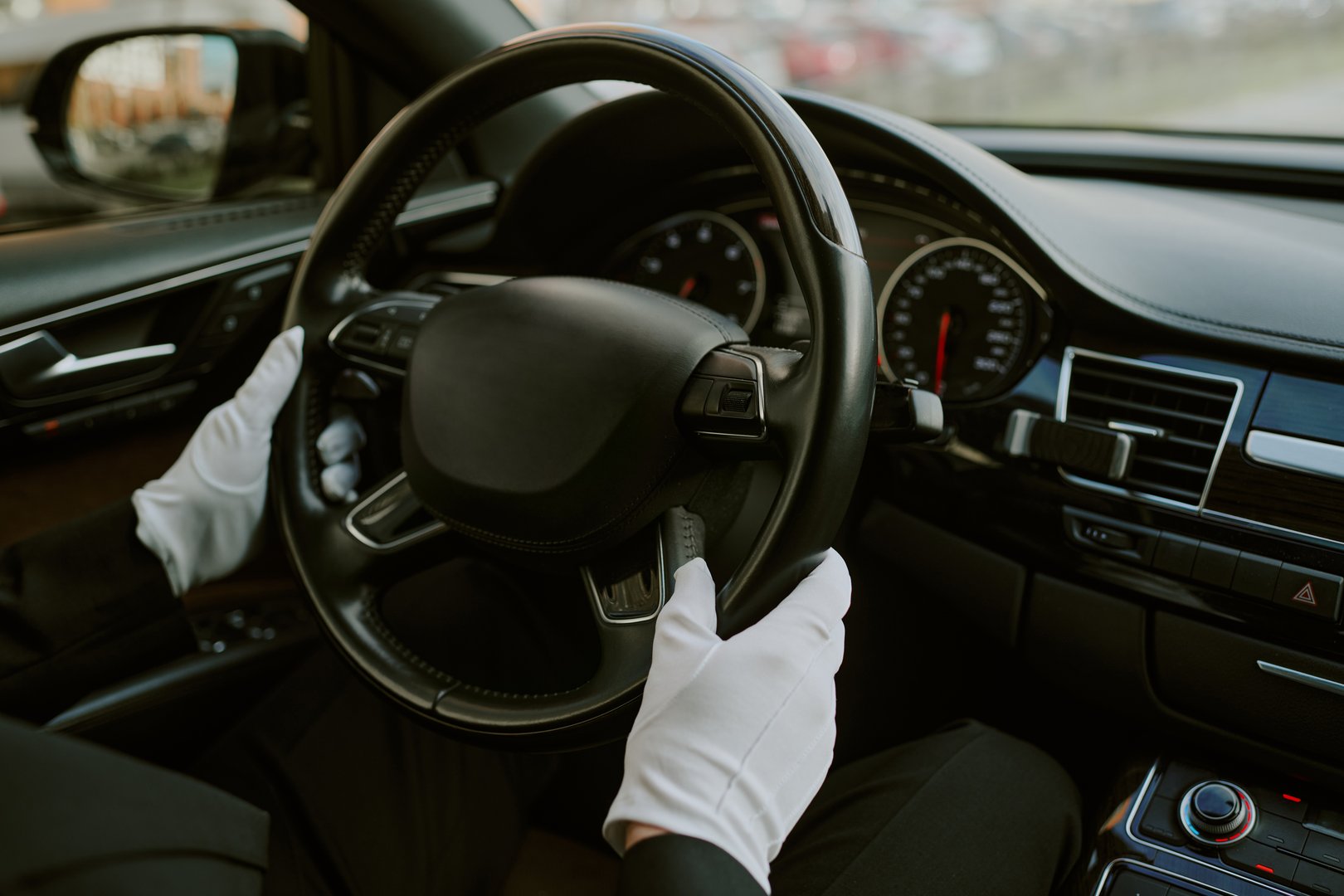 Caucasian middle aged man wearing gloves driving luxury car, hands gripping steering wheel, dashboard and instrument panel visible, professional chauffeur service concept