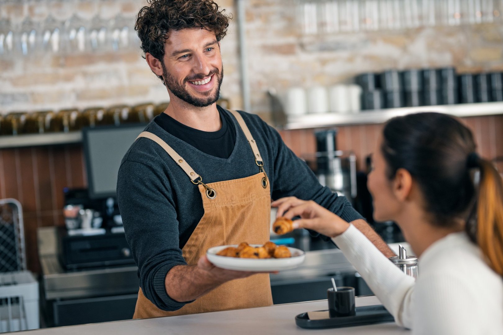 Shot of a handsome waiter talking with a client while serving chocolate croissants in the pastry shop.