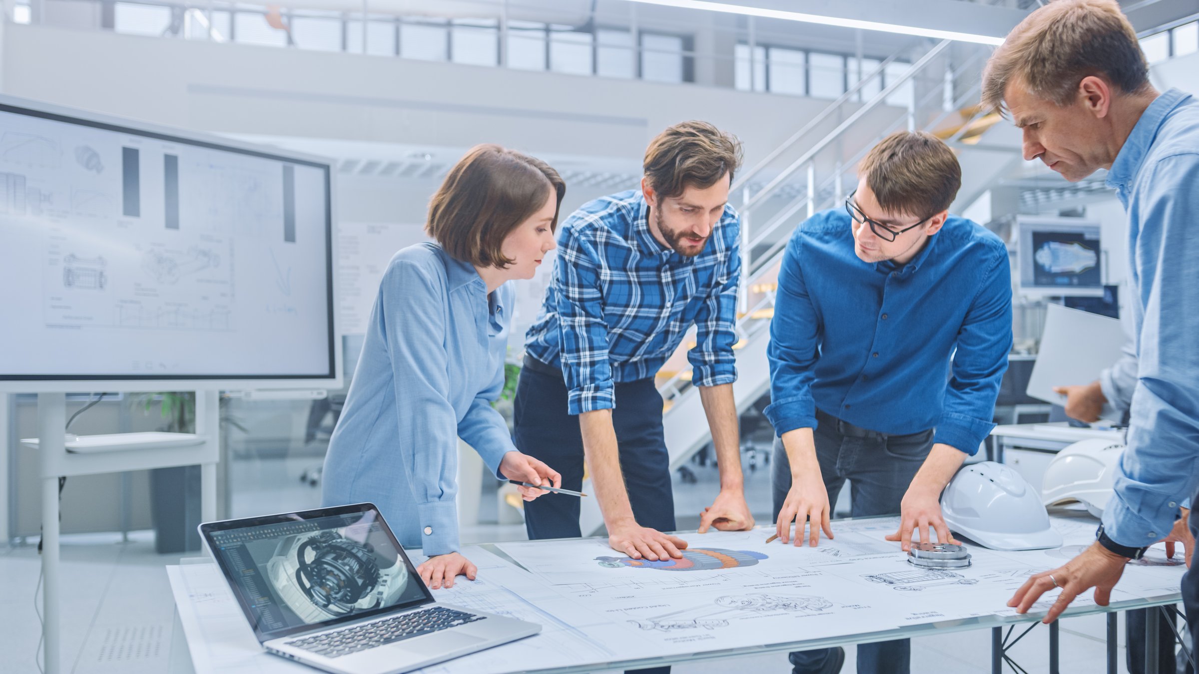 In the Industrial Engineering Facility: Diverse Group of Engineers and Technicians on a Meeting Gather Around Table with Engine Design Technical Drafts