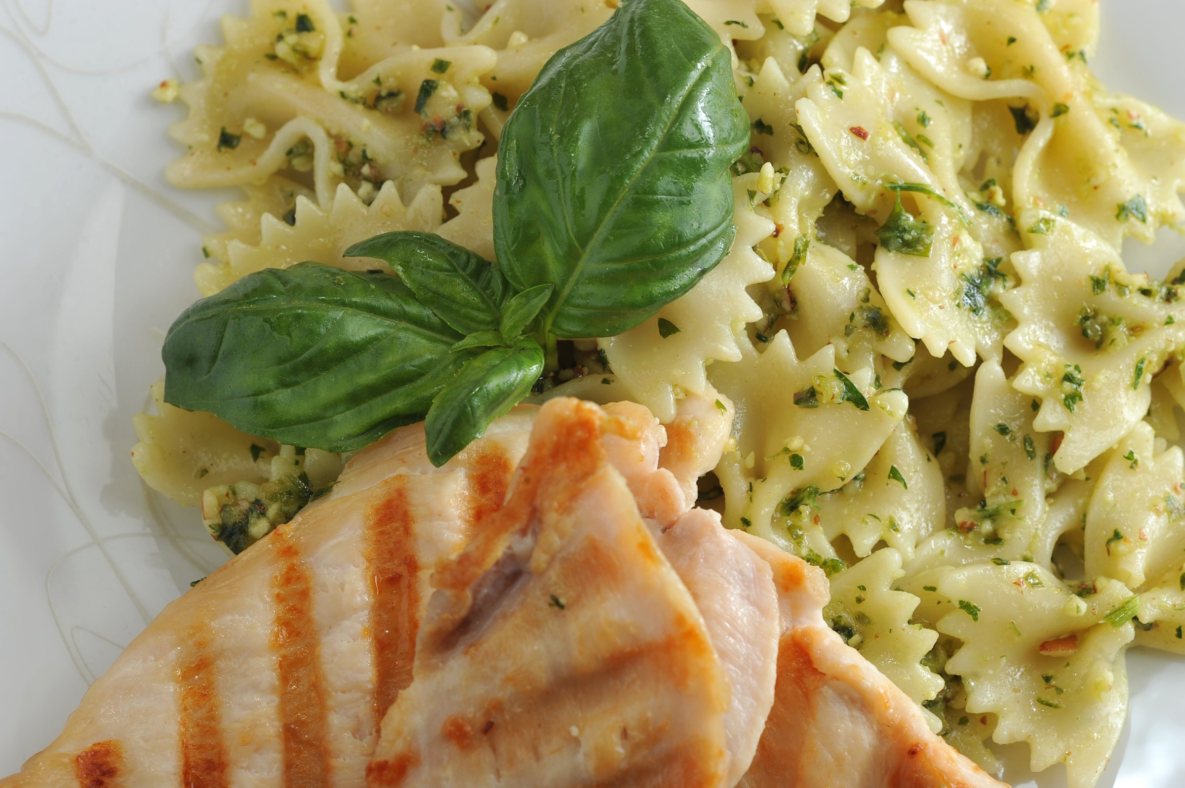 Pasta farfalle with pesto sauce. Next to the chicken meat, cooked on the grill. The dish is decorated with a leaf of fresh basil. View from above. Close-up.