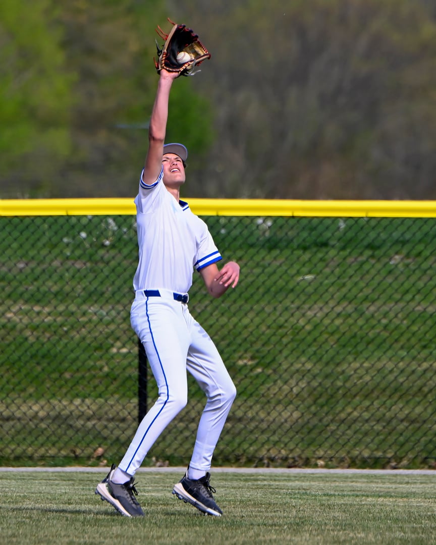 A teenage male baseball player catching a flyball with the ball in his glove