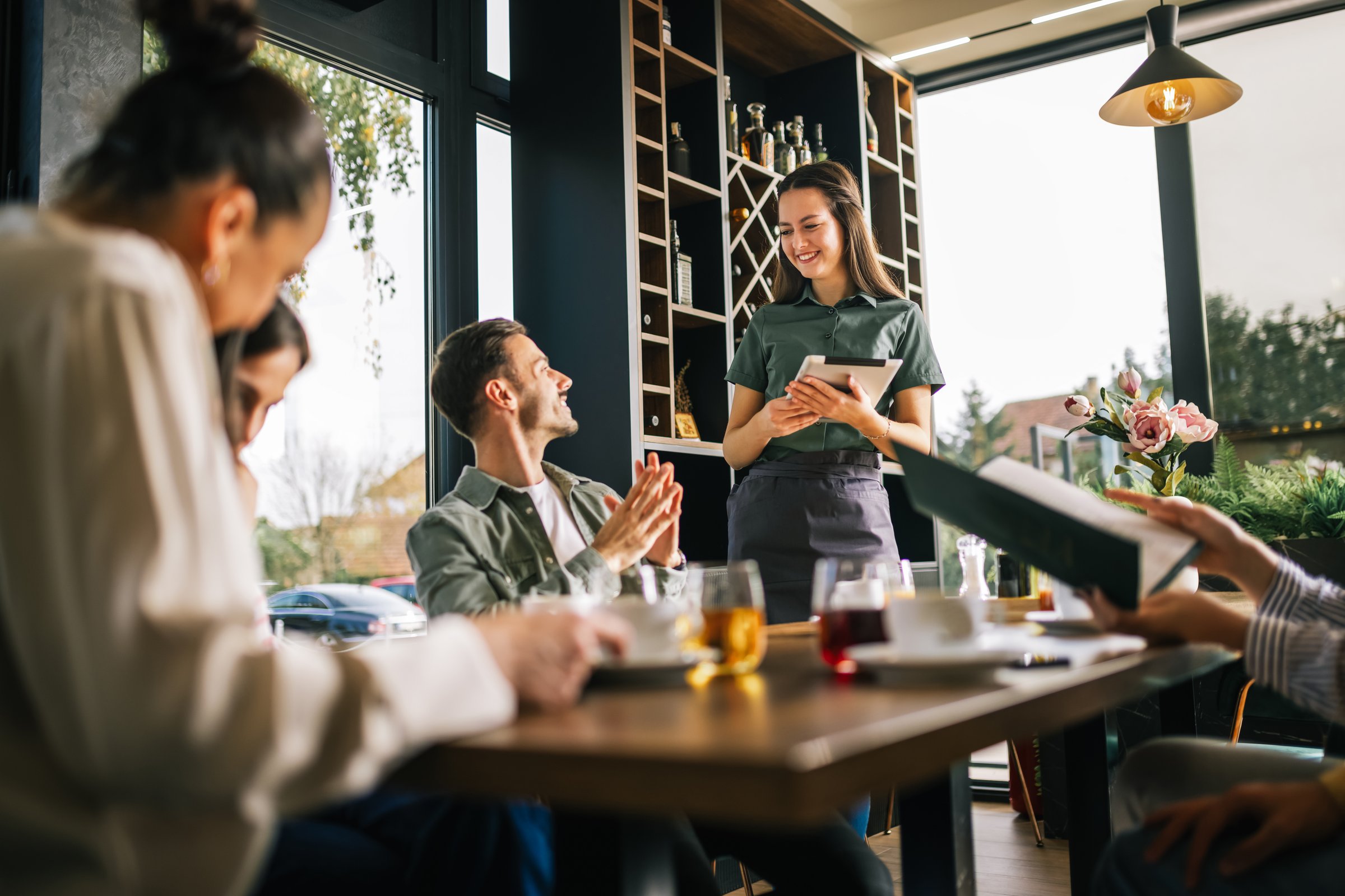 Group of people ordering food from the waitress. Waitress writing orders down on tablet. Undecided people reading the menu while the waitress waits and helps them.
