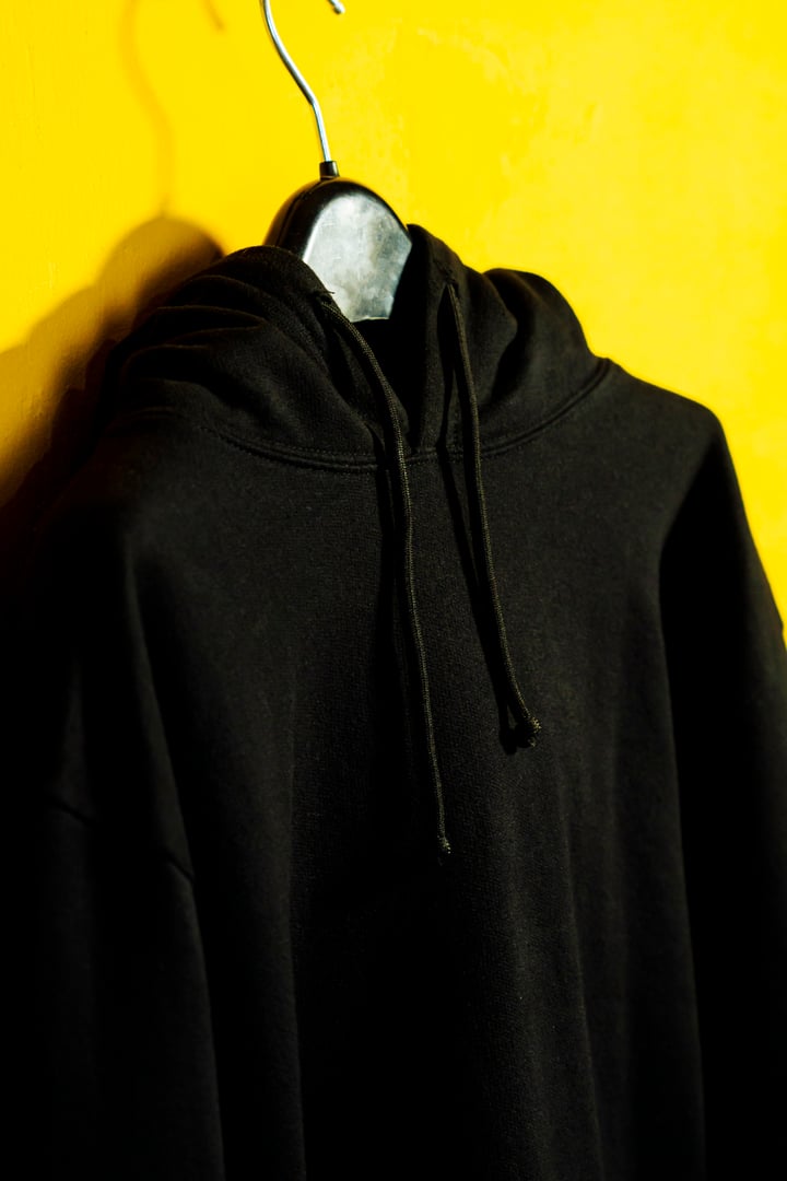 A minimalist fashion shot of a black hoodie hanging against a clean yellow background, creating a trendy and vibrant visual appeal.