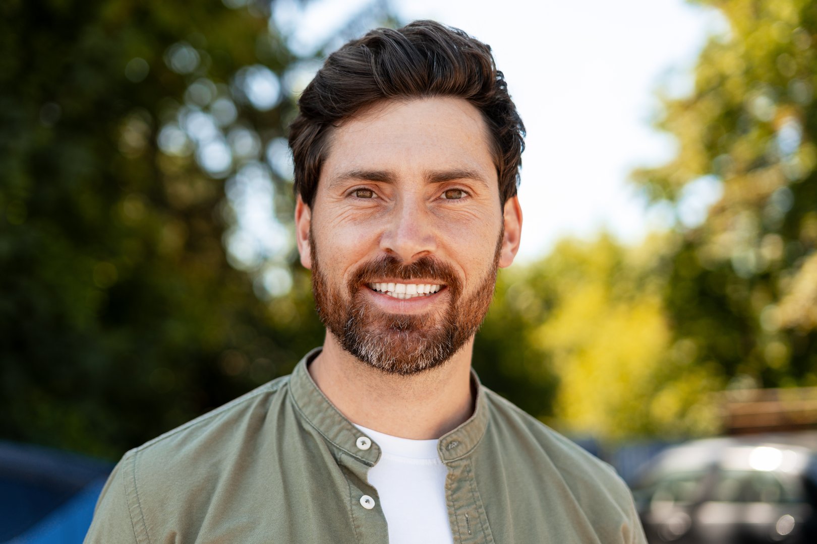 Headshot of a cheerful mid adult man with a beard, enjoying the outdoors and smiling at the camera