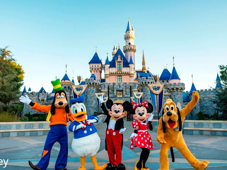Disney characters pose in front of Sleeping Beauty Castle at Disneyland, with Goofy, Donald, Minnie, and Pluto.