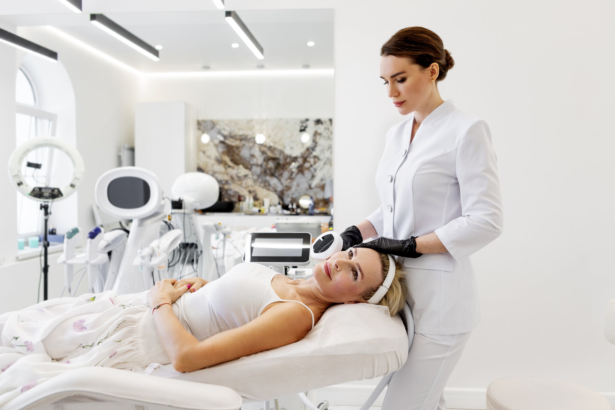 Cosmetologist using skincare equipment for photorejuvenation facial treatment. Mature woman lying on chair in beauty clinic before non-invasive anti-aging procedure with aesthetic laser technology