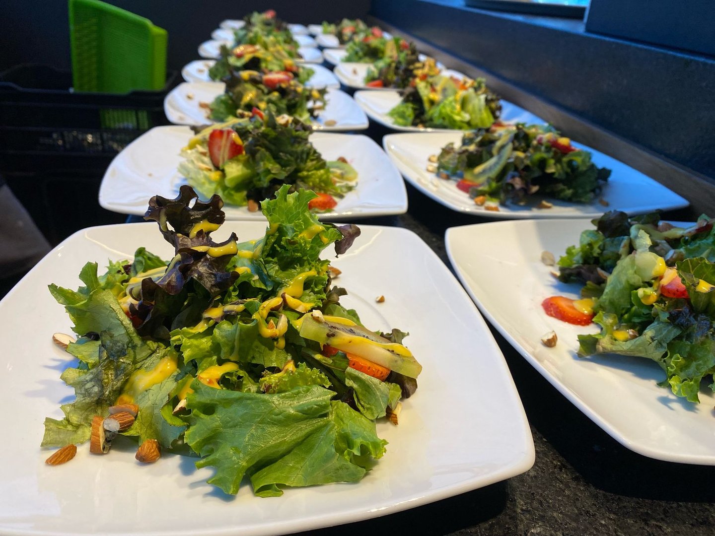 Plates of fresh garden salads with mixed greens, strawberries, nuts, and sliced zucchini, arranged in a restaurant setting.
