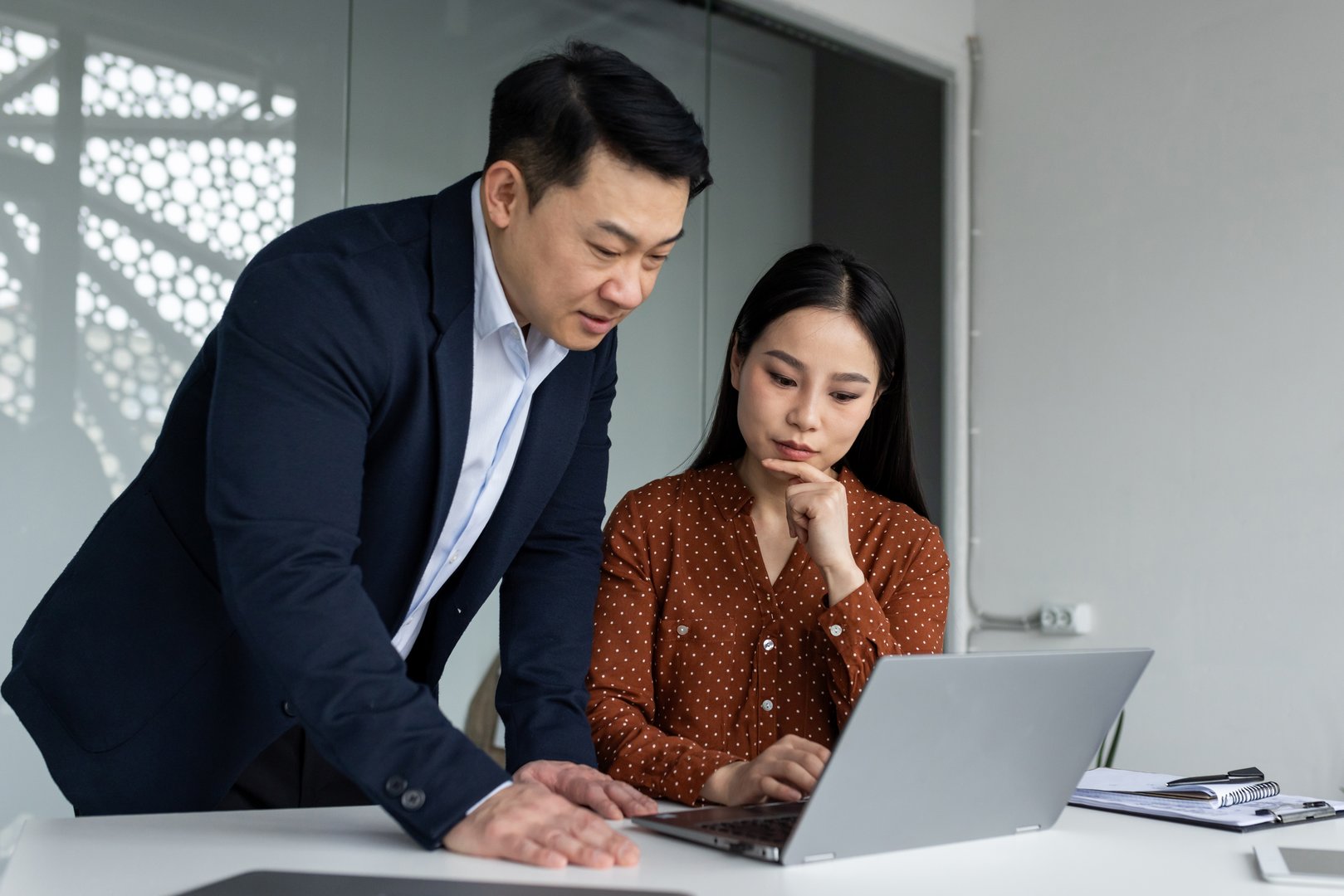 Business professionals engaged in discussion using laptop in modern office. Focused teamwork highlights collaboration and productivity. Professionals, male and female, reviewing project
