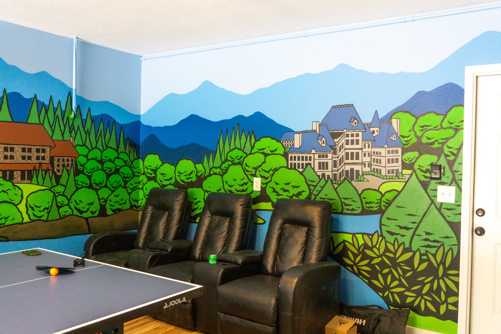 Room with a mountain mural, theater seating, and a ping pong table.