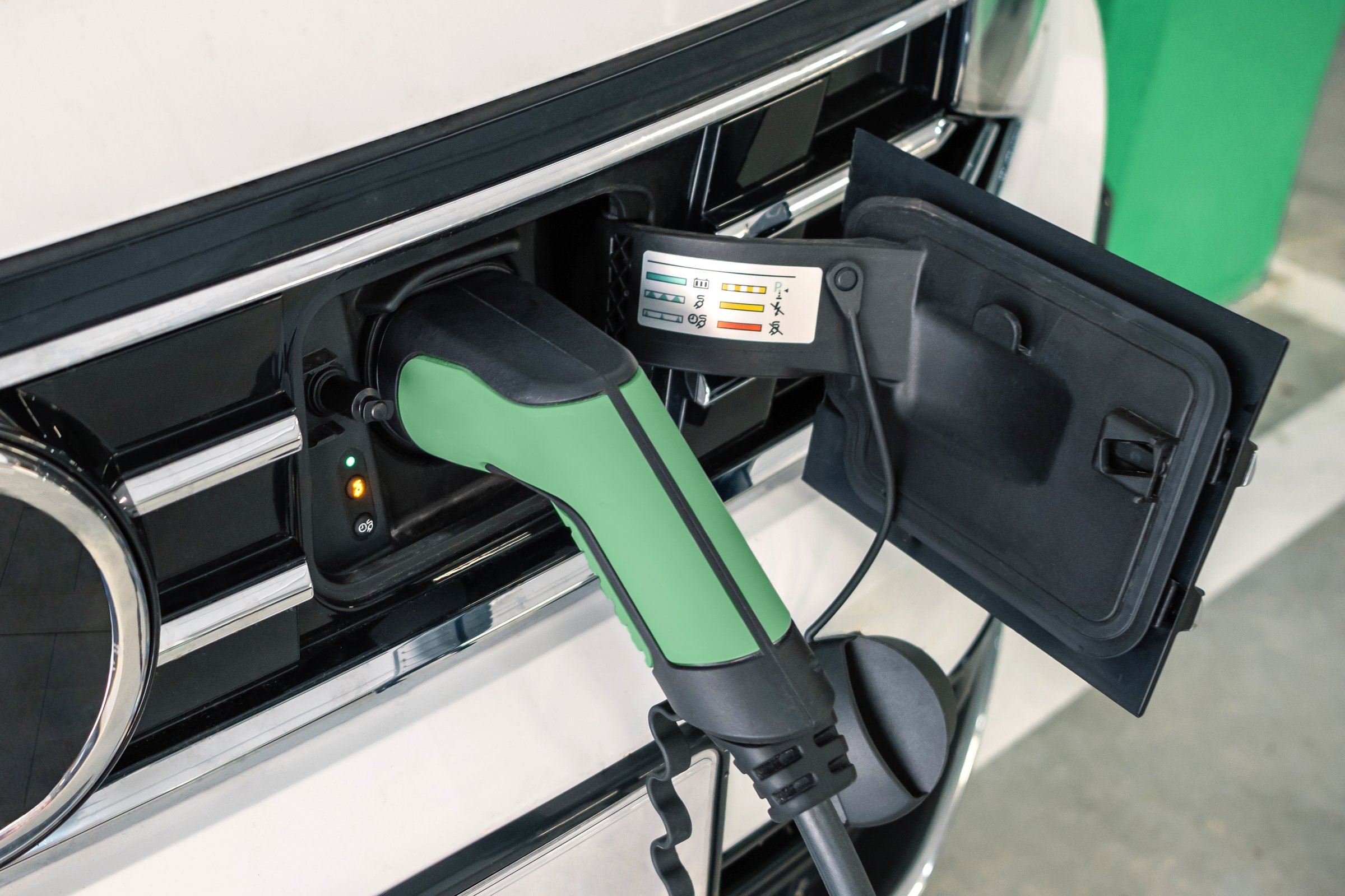 Green electric car charging at station, showcasing eco friendly transportation and promoting sustainable energy solutions for cleaner and greener future. Detail of socket plugged in hybrid vehicle.