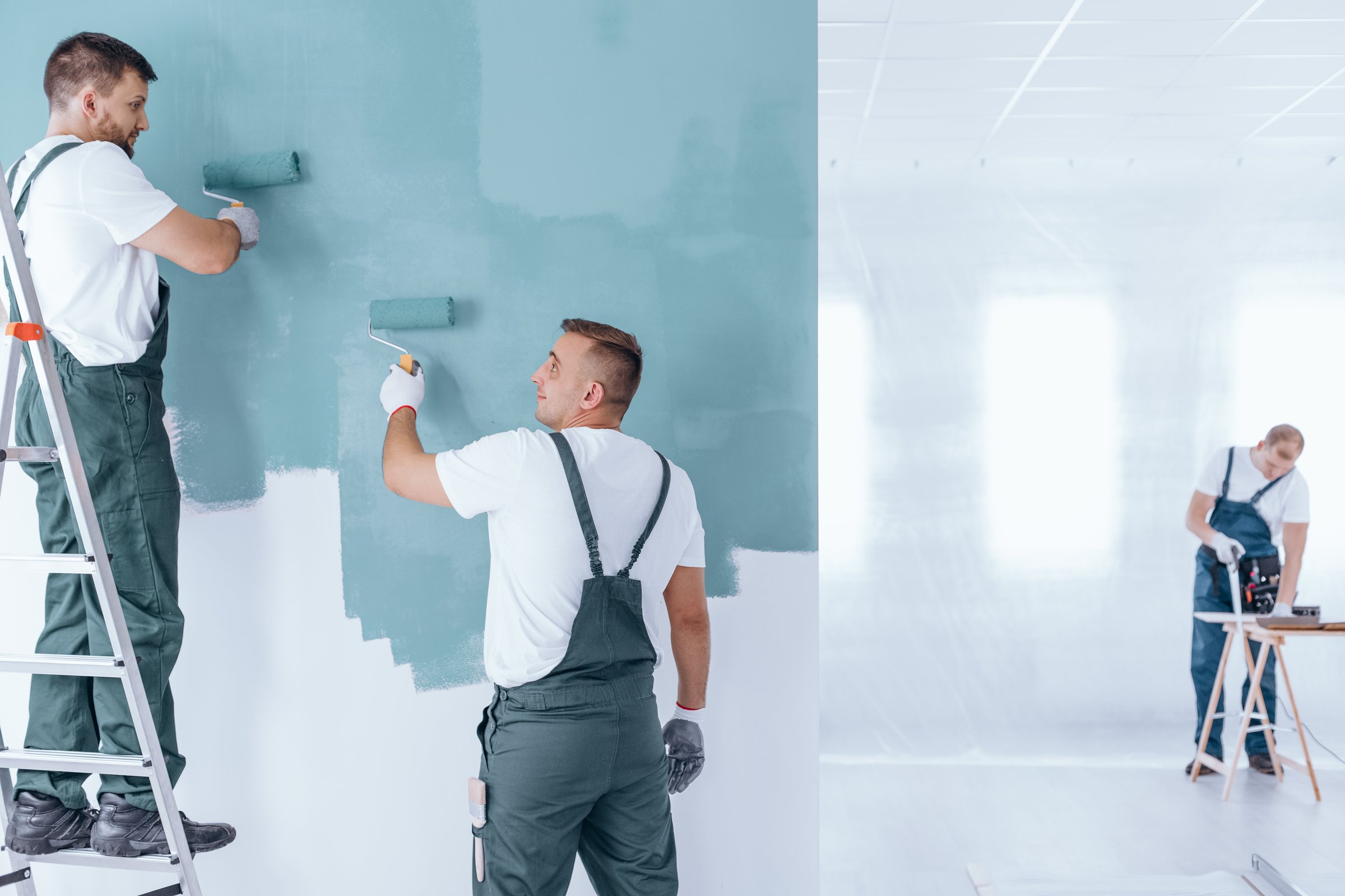 Men painting the wall in blue in empty home interior