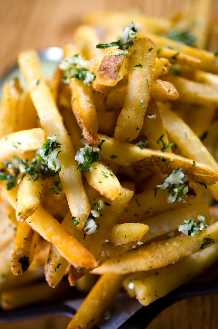 Golden crispy French fries topped with fresh parsley and garlic, stacked on a plate