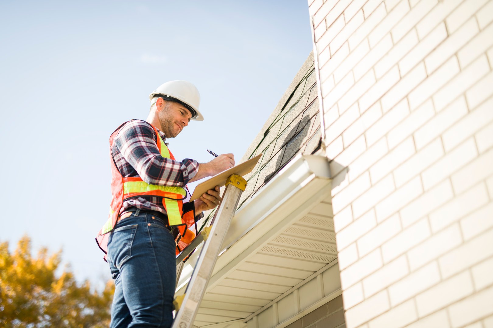 A man with hard hat standing on steps inspecting house roof