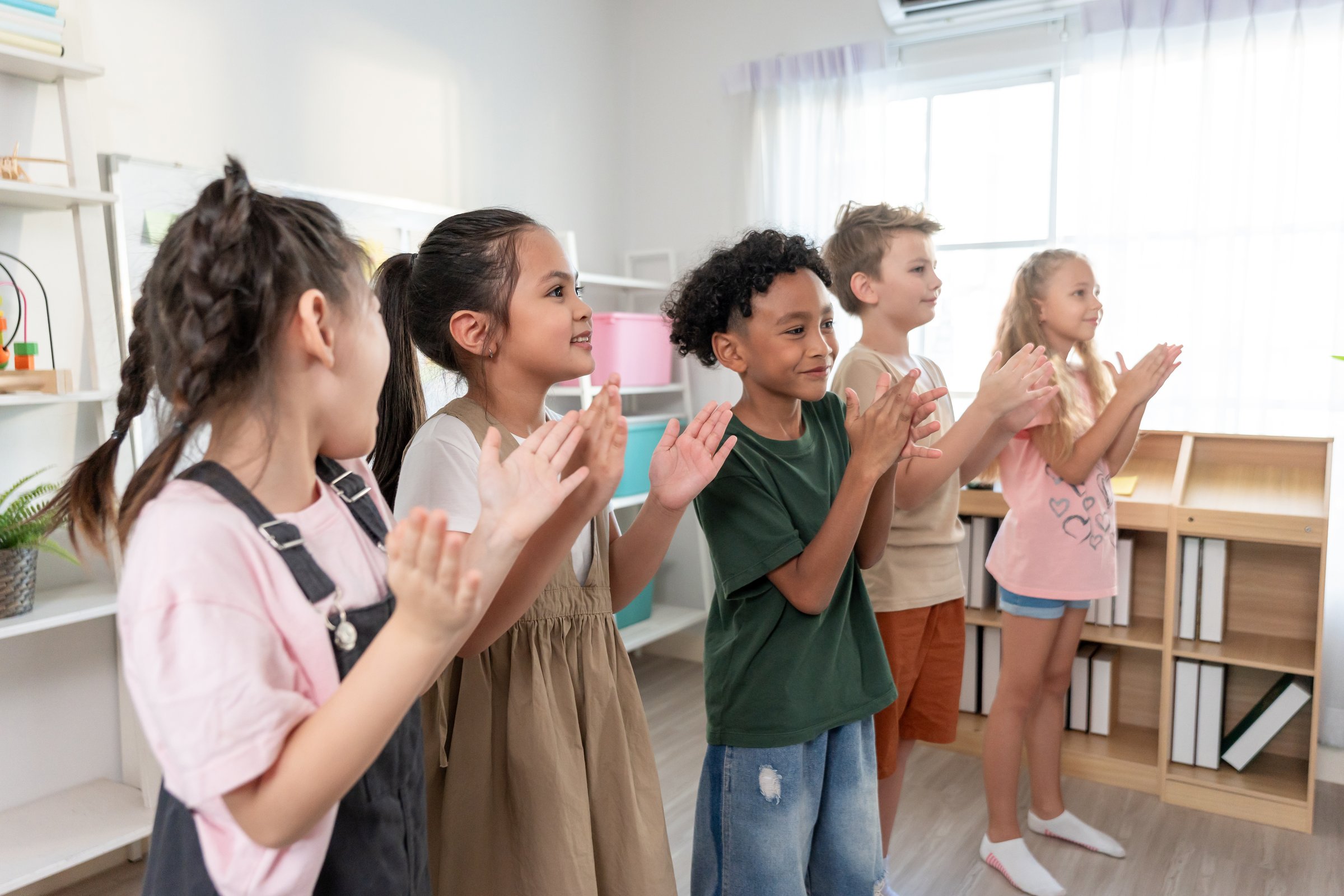 Group of diversity adorable student clapping hands at nursery school. Adorable schoolboy and girl feel happy and enjoy back to school, learning with teacher in classroom at elementary kindergarten.