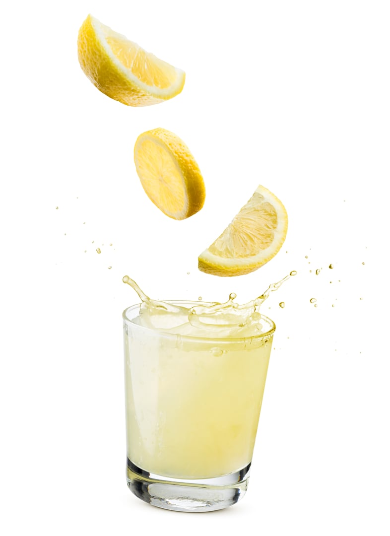 glass of lemonade with lemon slices falling, isolated on white background.