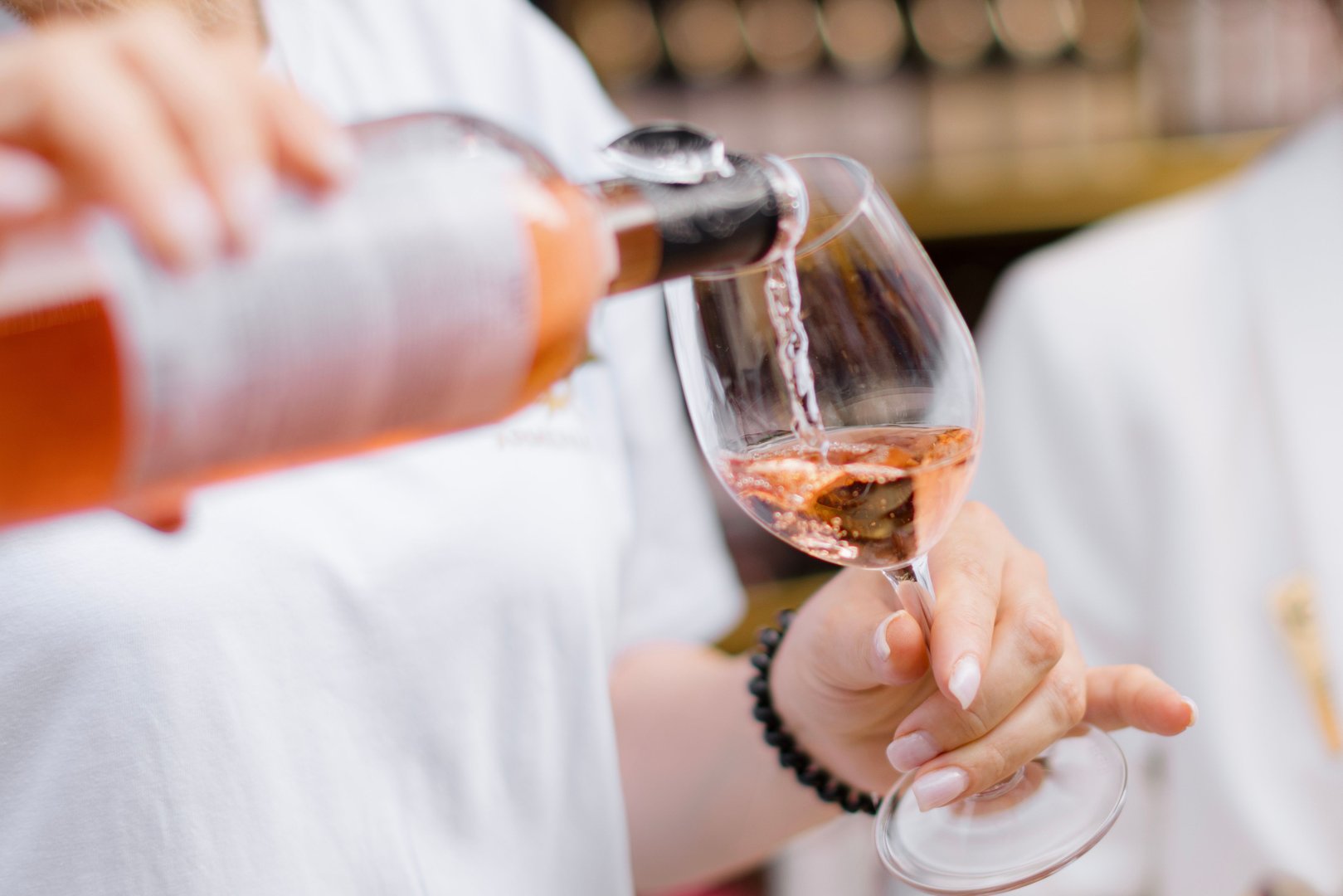 Close-up of a person pouring rose wine into a glass at an outdoor event, showcasing the elegance of the beverage.
