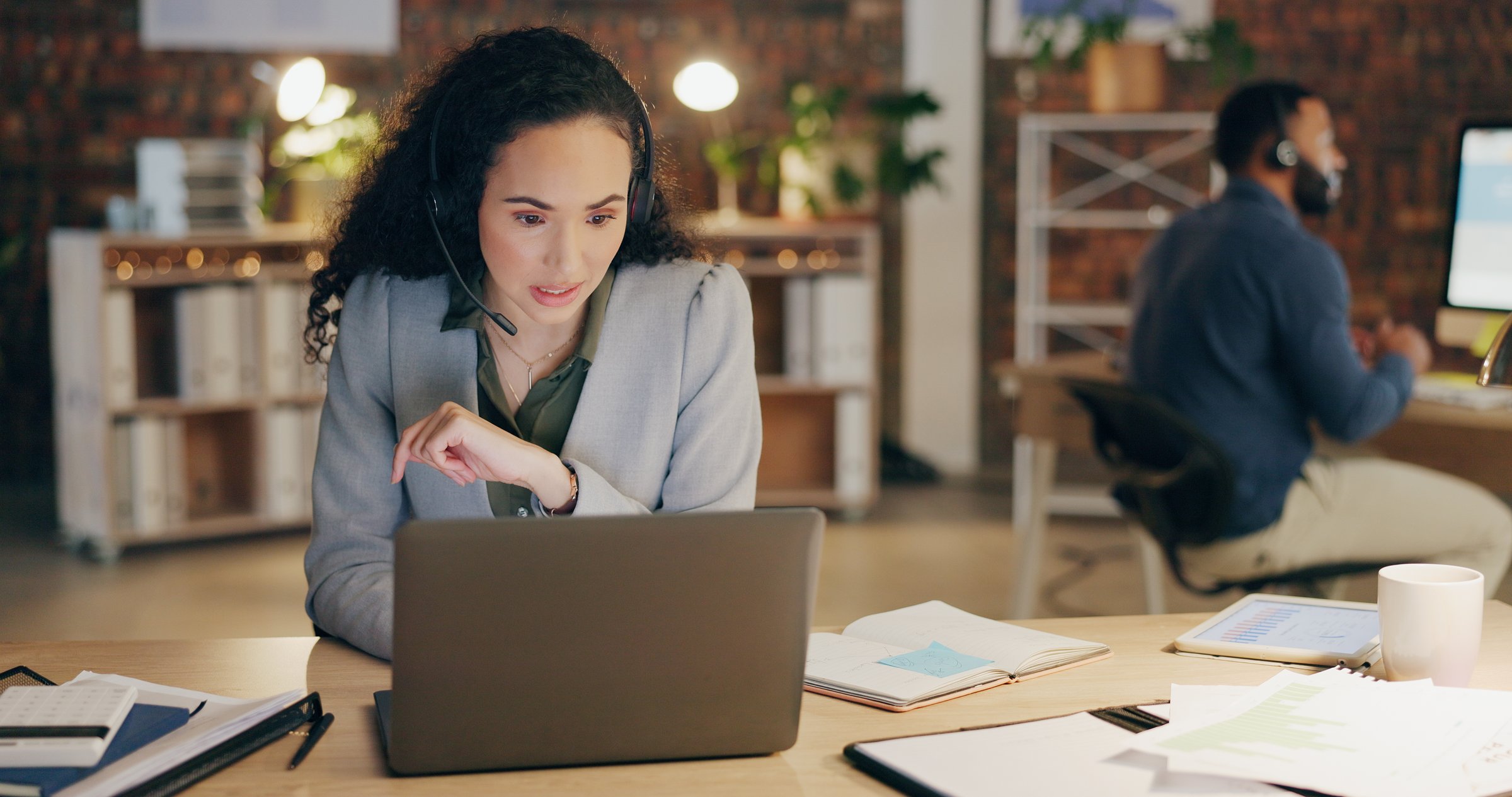 Telemarketing, business woman and laptop in office at night with conversation, customer support and virtual assistant. Headphones, discussion and call center agency with web consultation at desk