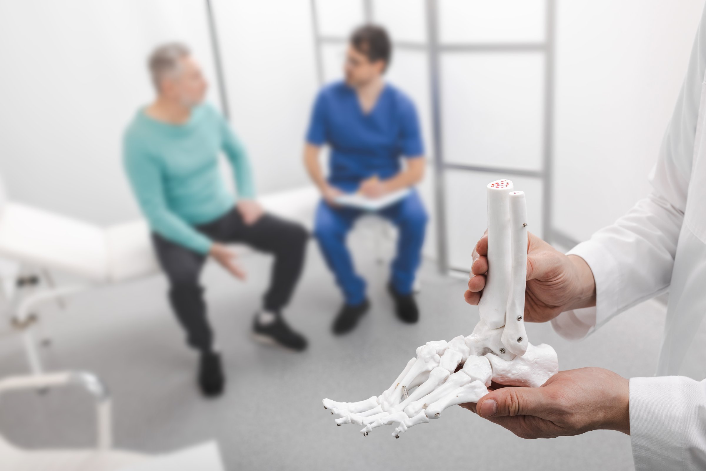Podiatrist showing anatomical foot skeleton model during his assistant examination injured leg of patient in department of traumatology and orthopedics