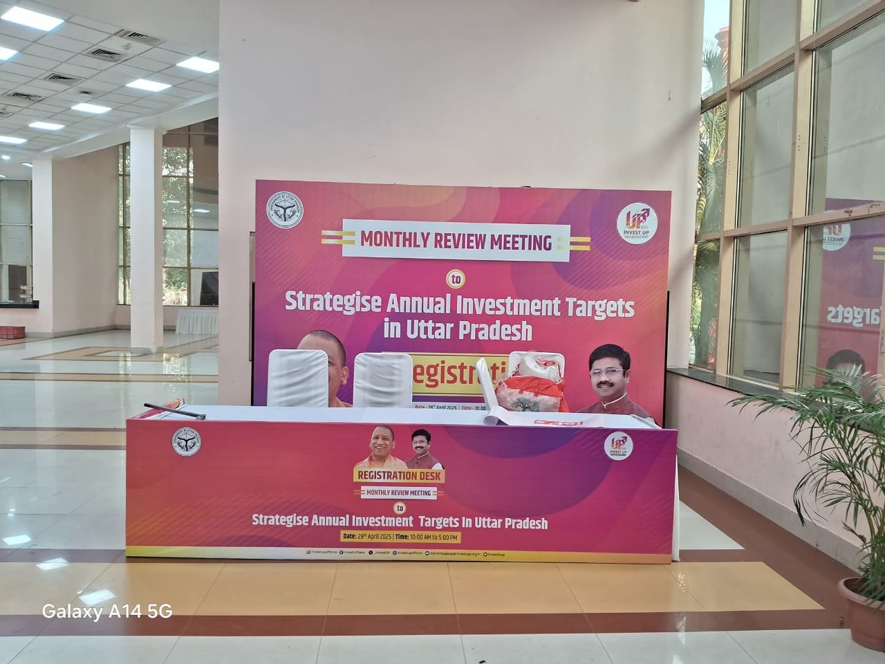 Registration desk for a meeting on strategic investment targets in Uttar Pradesh, with posters and banners displayed.
